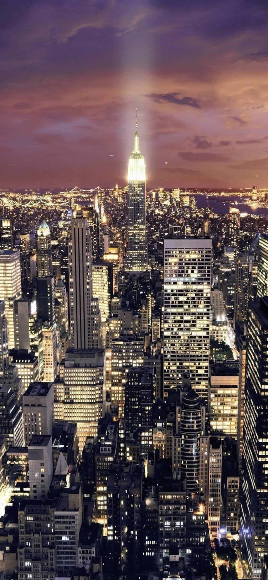 iPhone Xs New York 桌布 壁紙 — 暮色中高聳的城市景觀，帝國大廈在紫色和橙色的天空下閃耀著光芒。