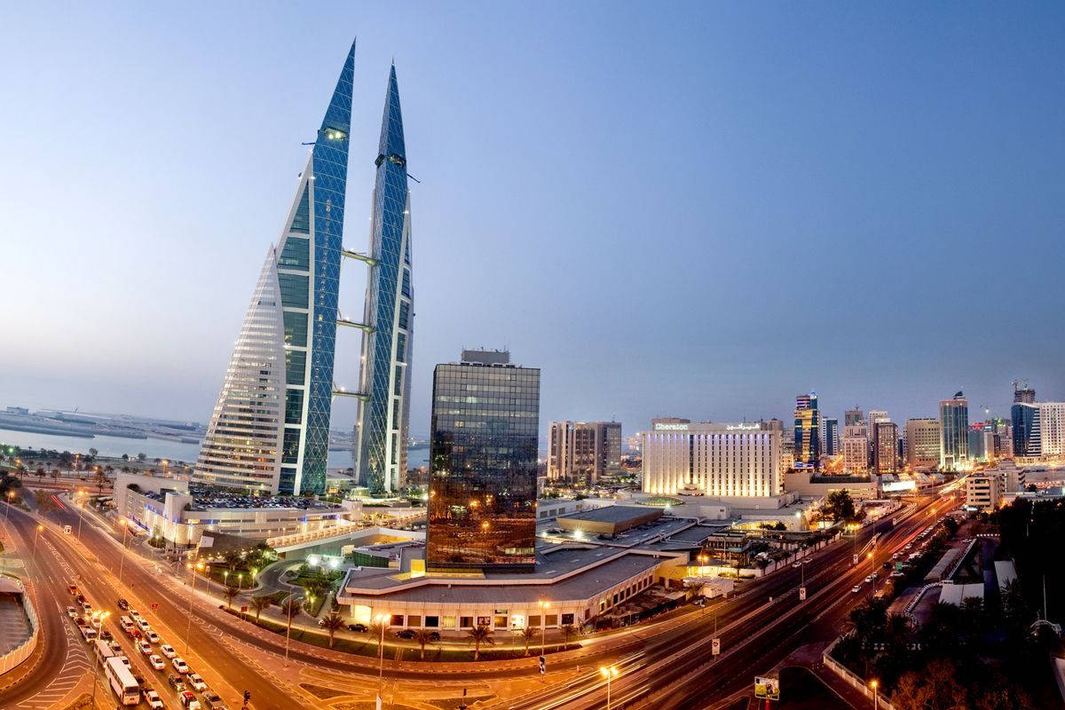 Bahrain 桌布 壁紙 — 暮色城市景觀，以標誌性的巴林世界貿易中心塔樓為特色，下方有發光的燈光和繁忙的道路。