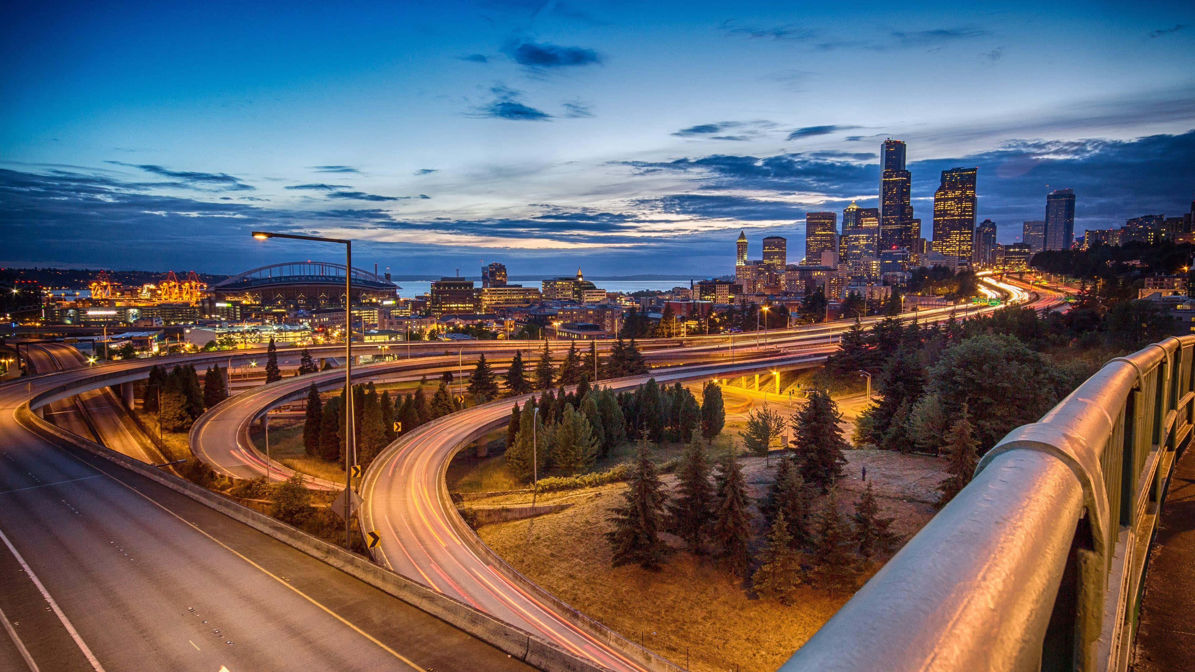 Seattle At Night 桌布 壁紙 — 暮色城市景觀，發光的摩天大樓和蜿蜒高速公路上的車流光跡。