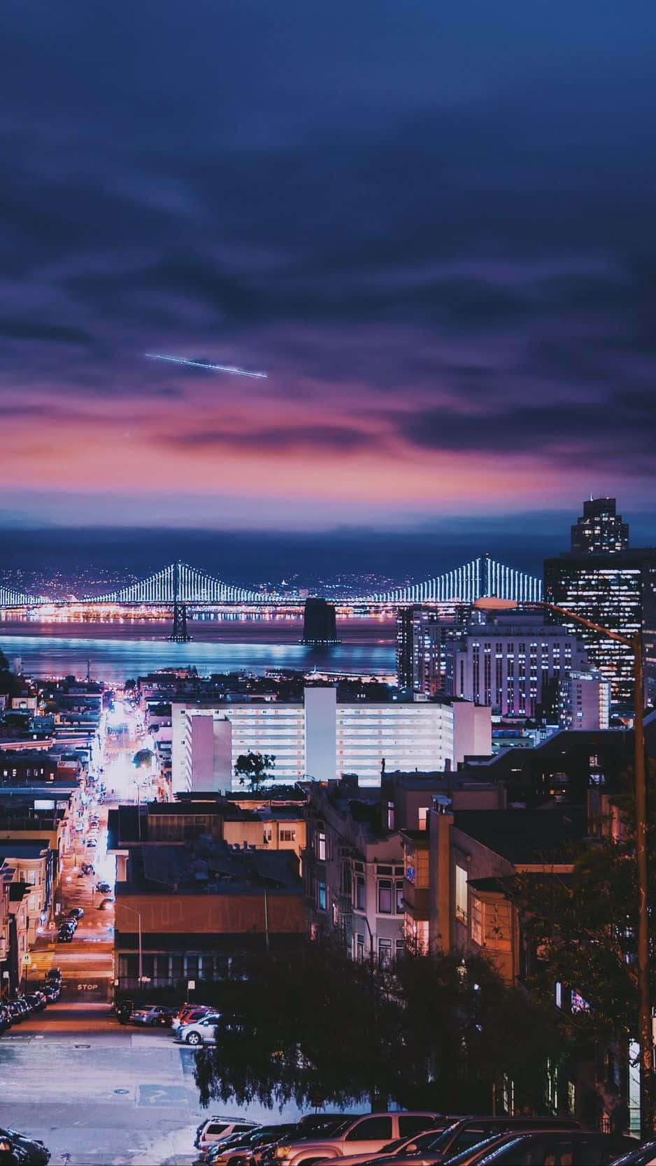 bridge 桌布 壁紙 — 暮色城市景觀，紫色和粉紅色天空下，水面上有一座發光的橋樑，下方是燈火通明的街道。