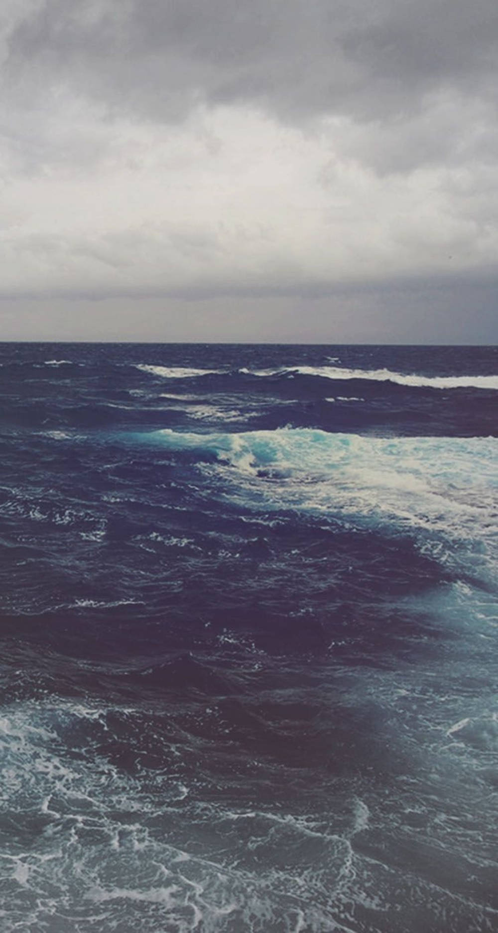 Ocean iPhone 桌布 壁紙 — 暴風雨中的海洋，黑暗的波浪在沉重的灰色天空下翻騰。