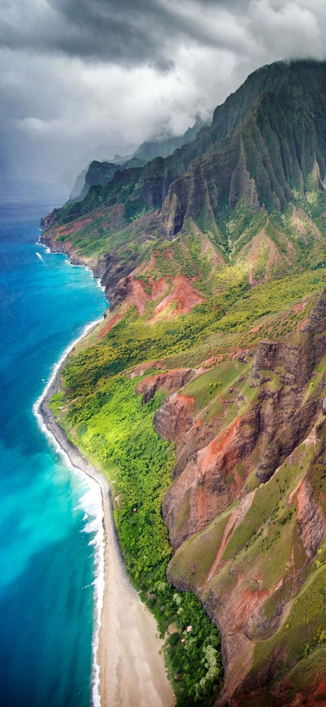 Hawaiian 桌布 壁紙 — 暴風雨天空下，碧綠海洋波浪拍打沙灘的戲劇性海岸懸崖鳥瞰圖。