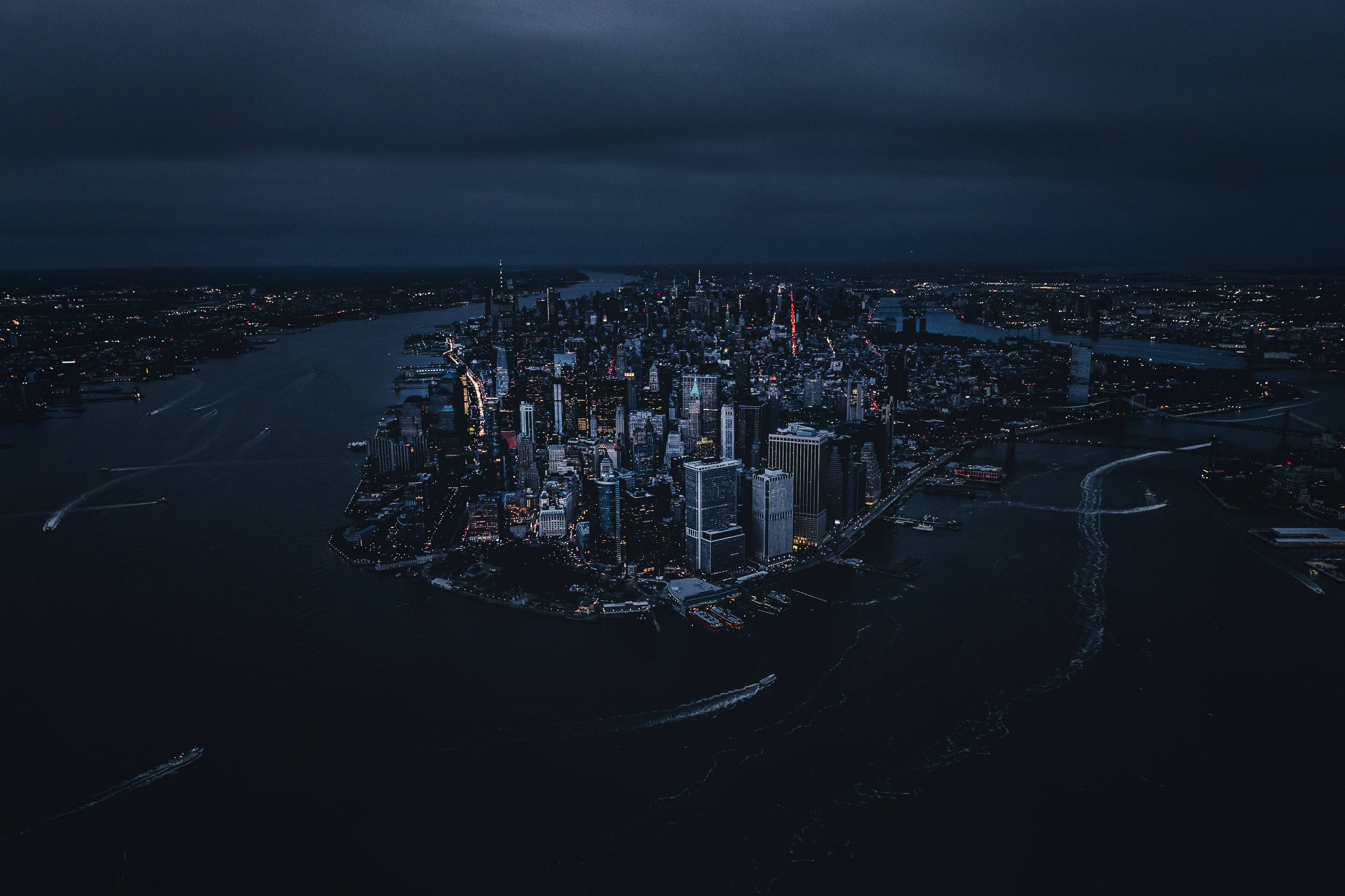 4K New York City 桌布 壁紙 — 暴風雨天空下，閃爍摩天大樓與黑暗水域的廣闊城市夜景鳥瞰圖。