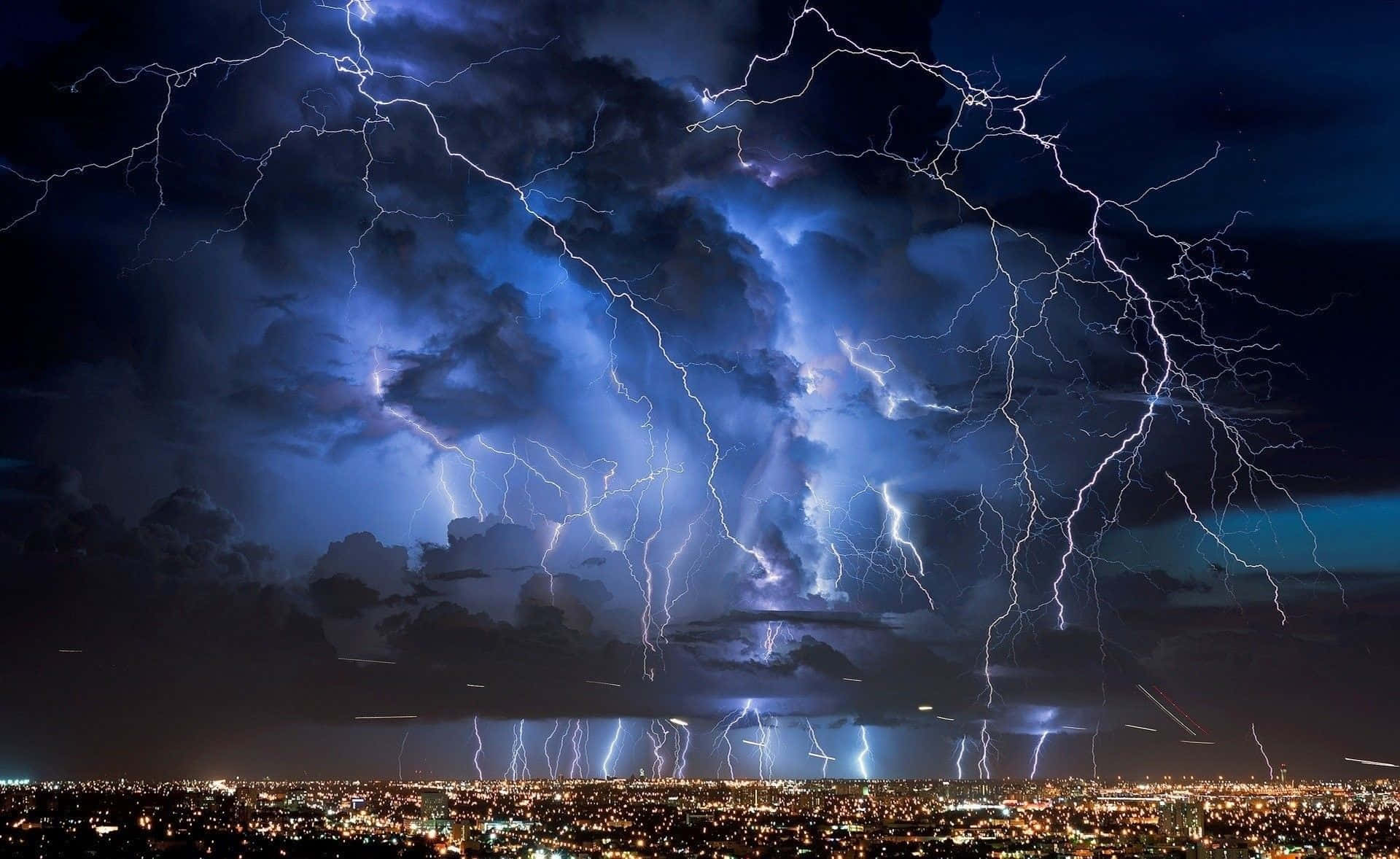 Lighting Bolt 桌布 壁紙 — 暴風雨天空下的城市景觀，被強烈的藍色閃電照亮，照亮了烏雲。