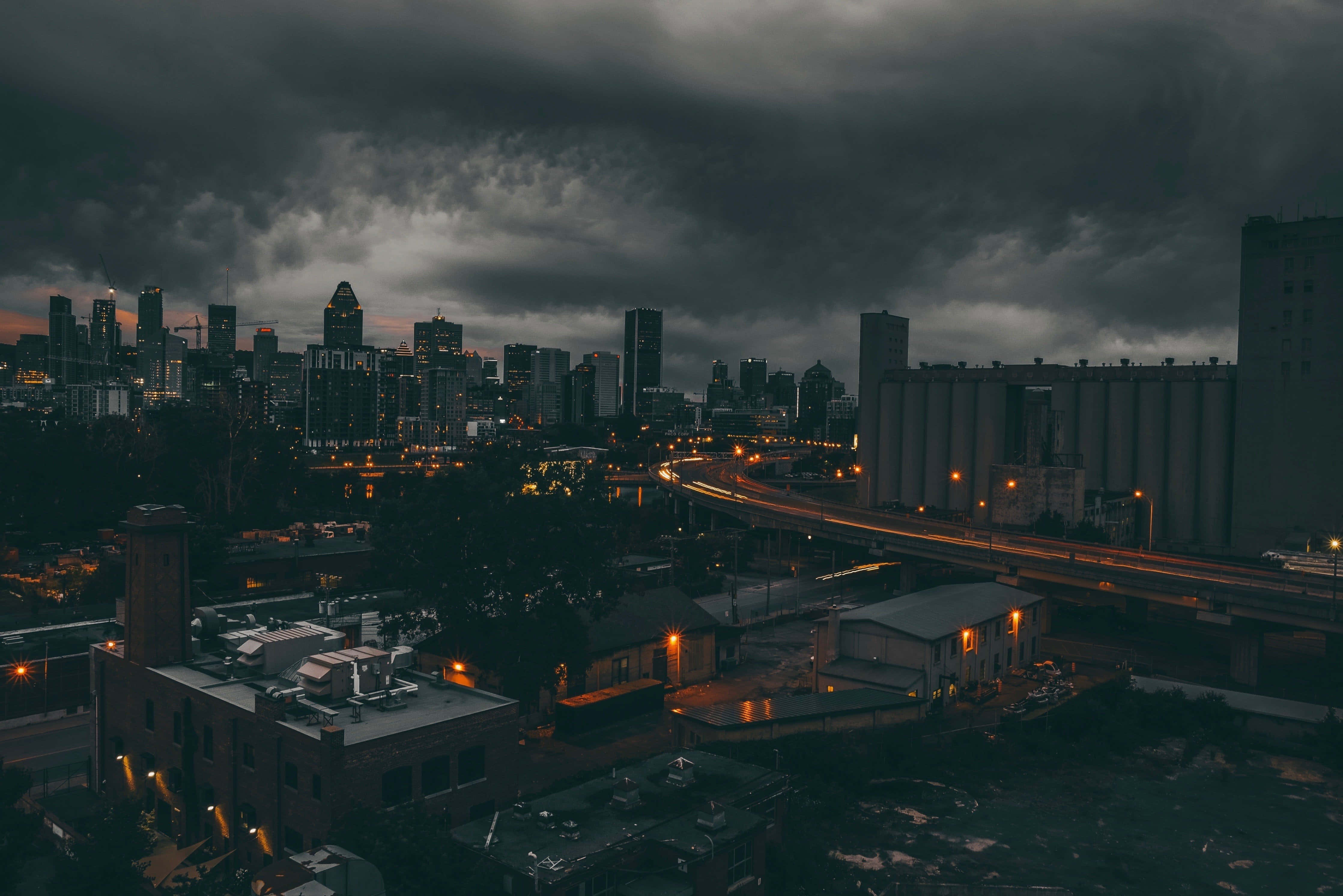 雲朵 桌布 壁紙 — 暴風雲下，黃昏時分發光街燈和高速公路線條構成的戲劇性城市天際線。