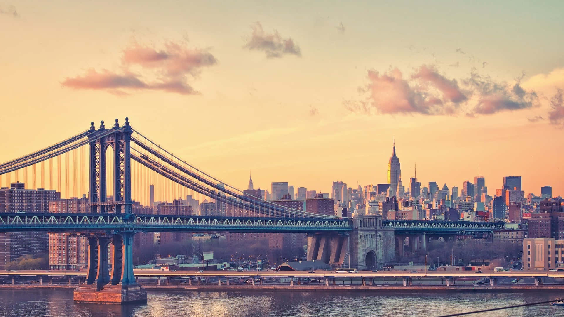 New York 桌布 壁紙 — 曼哈頓天際線在日落時分，布魯克林大橋橫跨水面，沐浴在溫暖的金色光芒中。