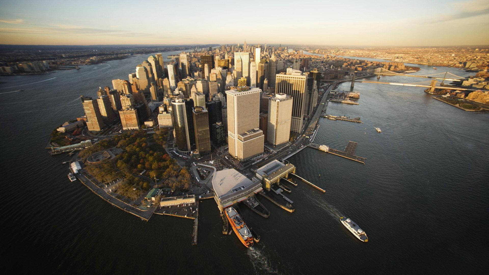 manhattan 桌布 壁紙 — 曼哈頓黃金時刻的鳥瞰圖，摩天大樓將溫暖的光線反射到周圍的水道上。