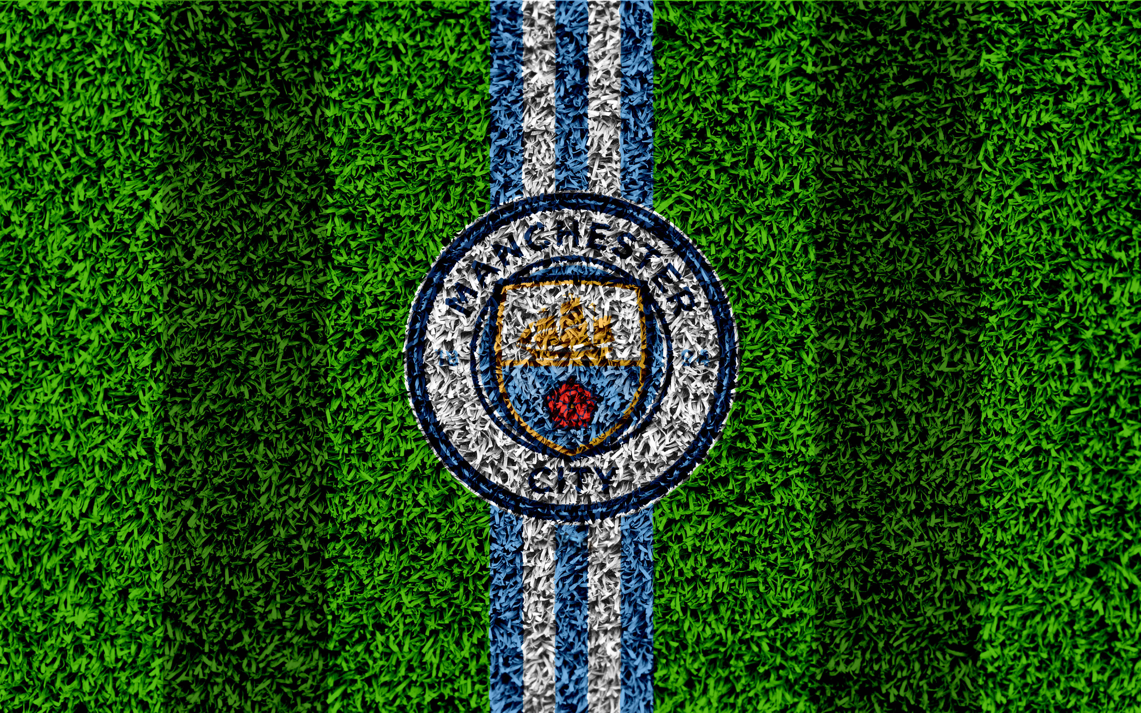 Manchester United Logo 桌布 壁紙 — 曼城足球俱樂部徽章繡在帶有藍白條紋的鮮綠色足球場草地上。