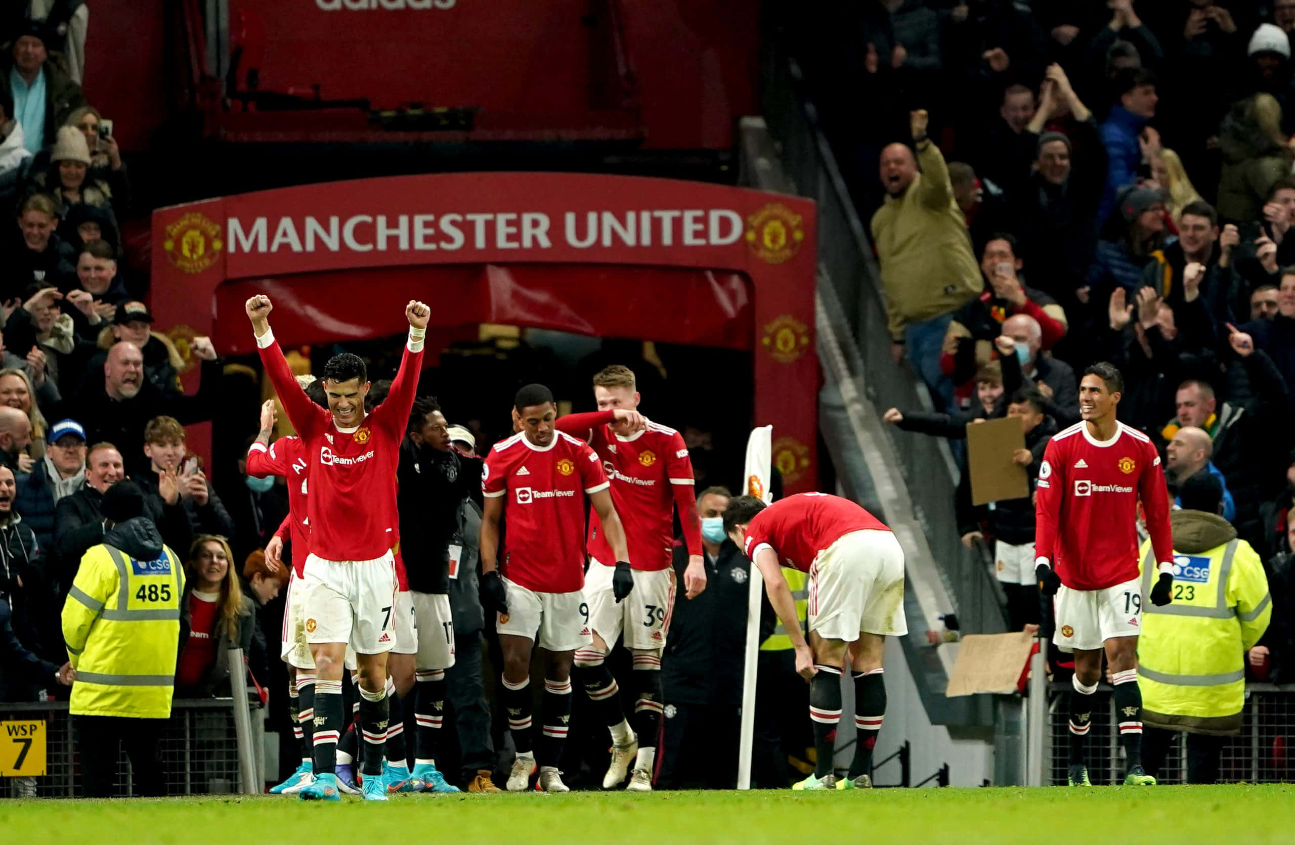 Manchester United Team 桌布 壁紙 — 曼聯球員在球場上慶祝勝利，球迷在紅色球會標誌後方的看台上歡呼。