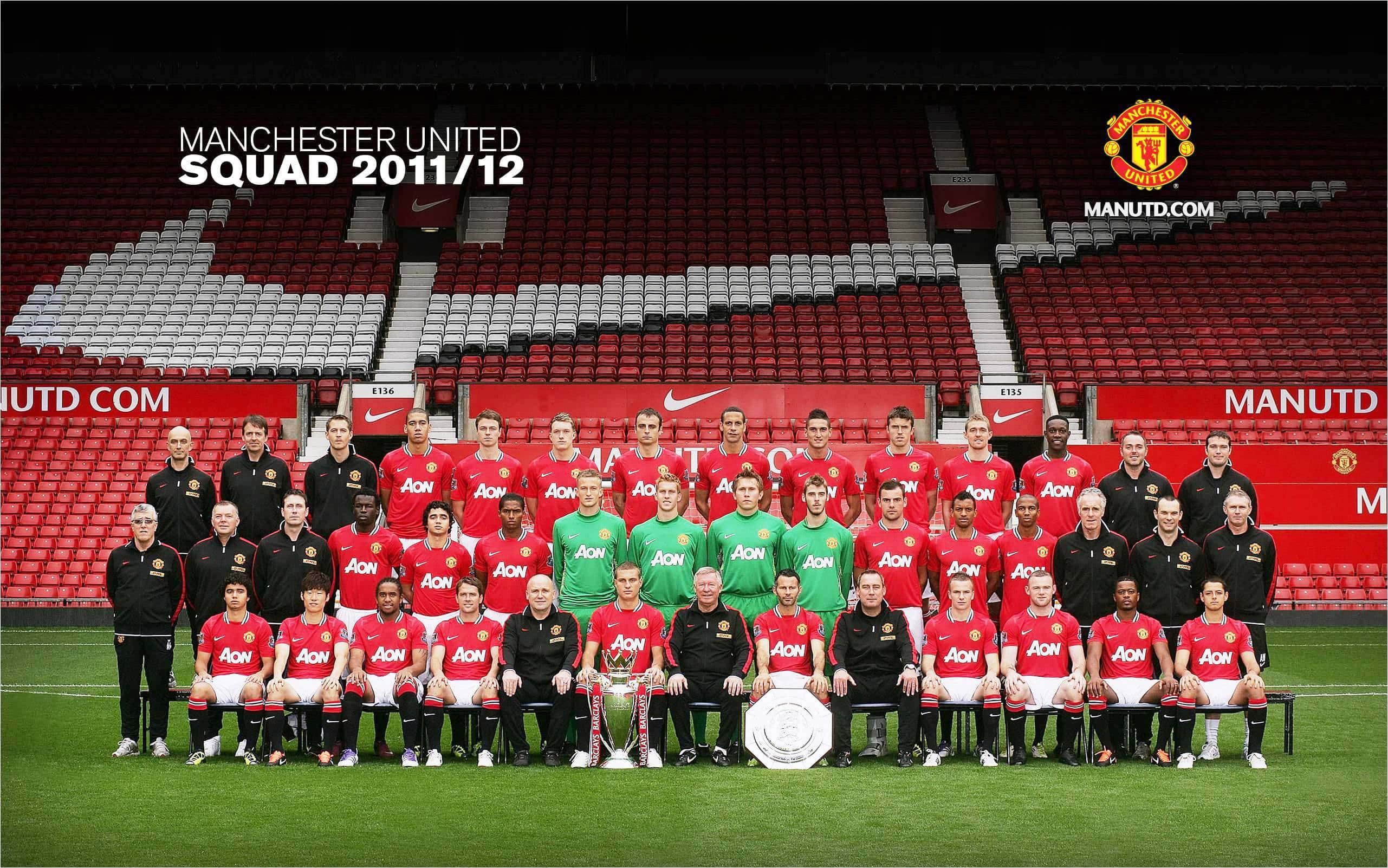 Manchester United Team 桌布 壁紙 — 曼聯足球隊身穿紅色球衣，在綠色球場上擺姿勢，身後是空無一人的紅色球場座位。
