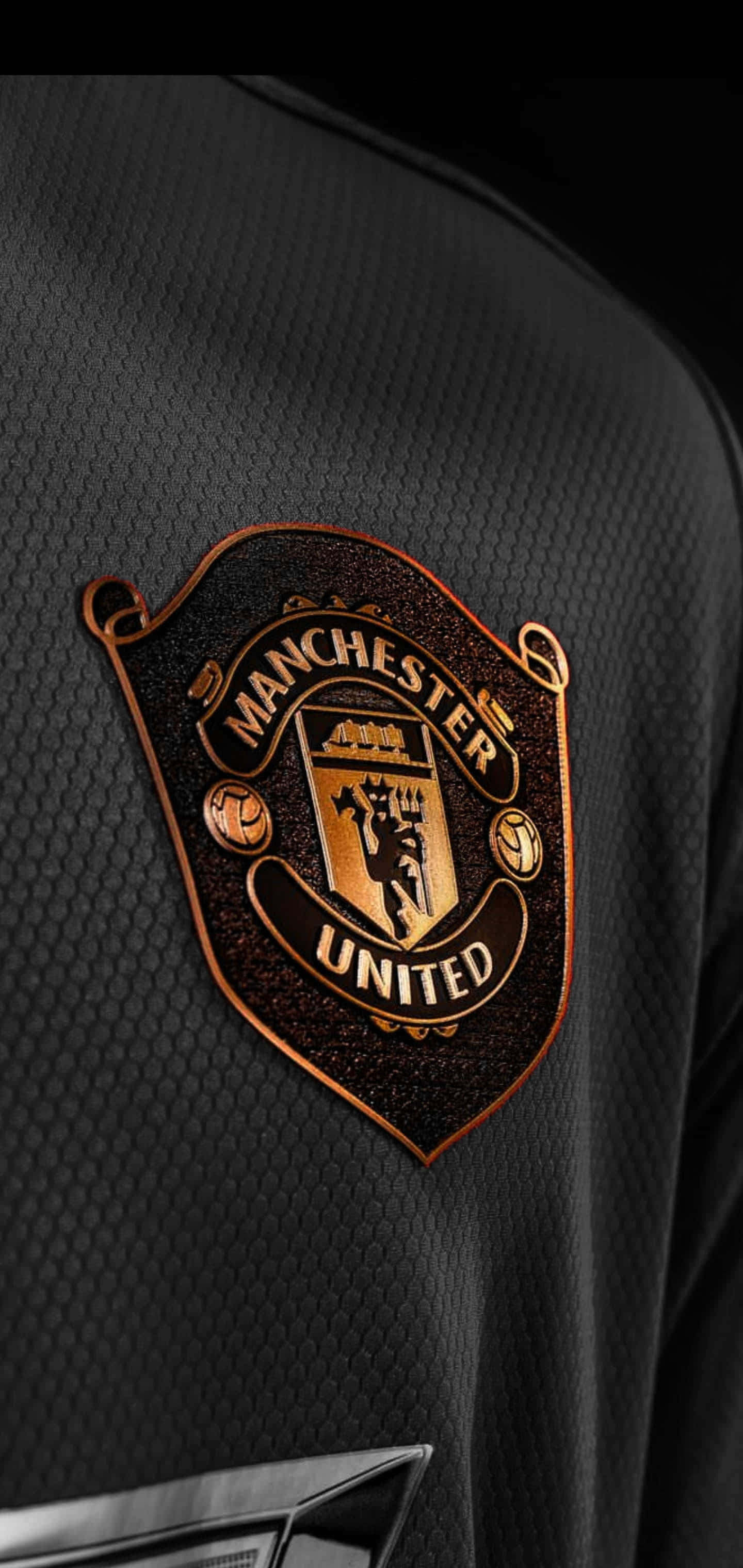 Manchester United iPhone 桌布 壁紙 — 曼聯金色會徽刺繡在黑色紋理足球球衣上的特寫。