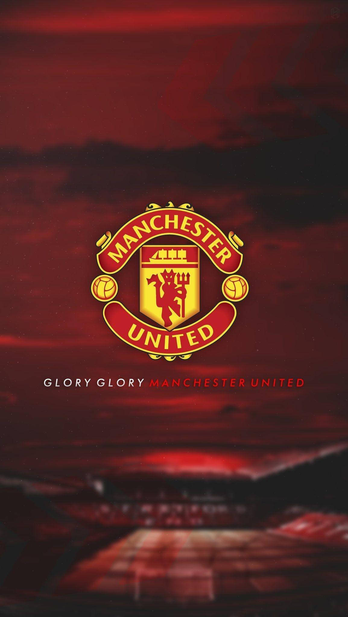 Manchester United Logo 桌布 壁紙 — 曼聯隊徽在紅色和金色中閃耀，背景是模糊球場上方戲劇性的暴風雨天空。