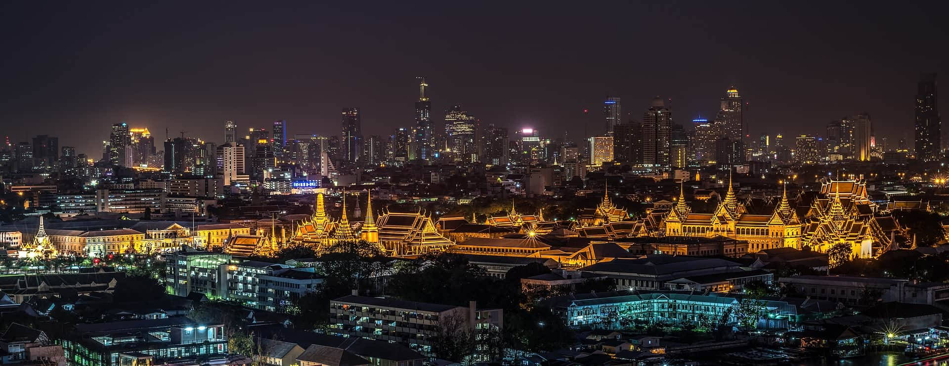 Bangkok 桌布 壁紙 — 曼谷天際線的 panoramic 夜景，現代摩天大樓與金色寺廟尖塔在黑暗天空下交融。