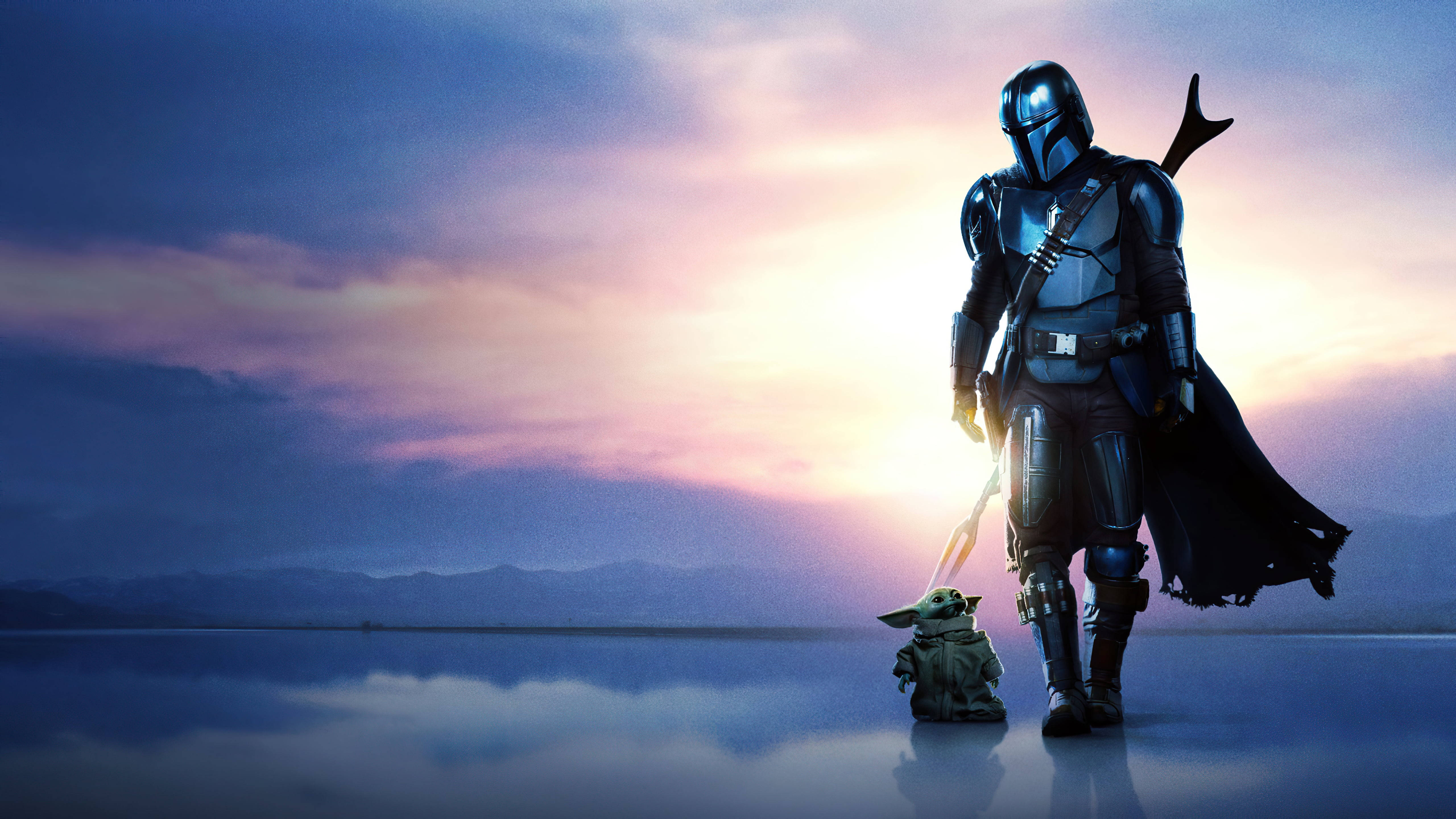 Mandalorian And Baby Yoda 桌布 壁紙 — 曼達洛人與古古在平靜如鏡的湖面和遠山之上，以燦爛的日落為背景，形成剪影。