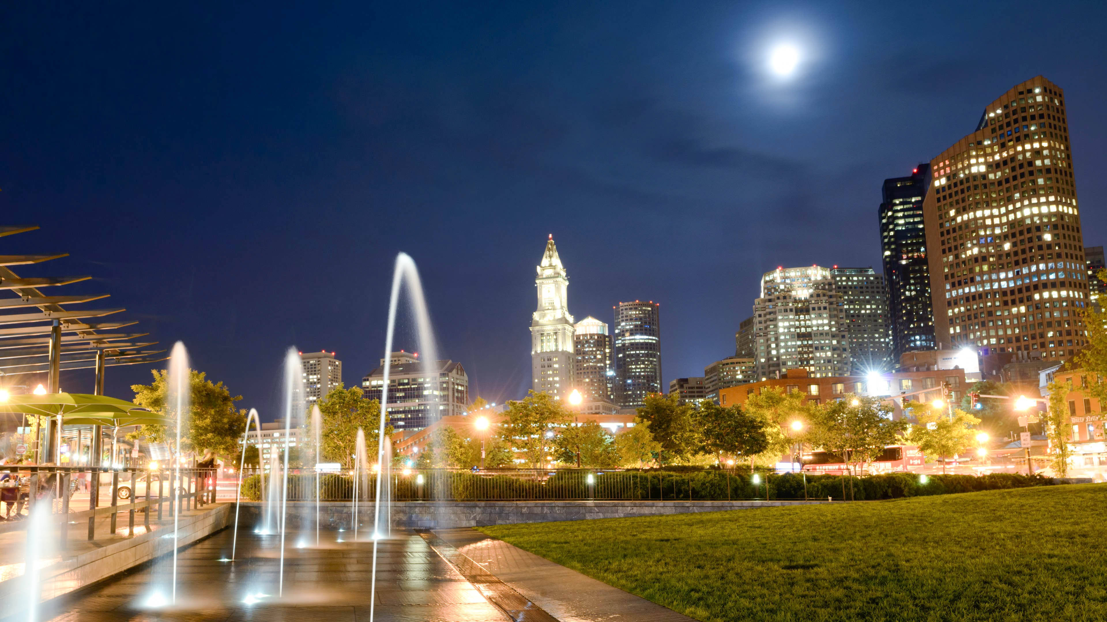 Boston 桌布 壁紙 — 月光下的城市天際線夜景，前景公園中有發光的摩天大樓和閃爍的噴泉。