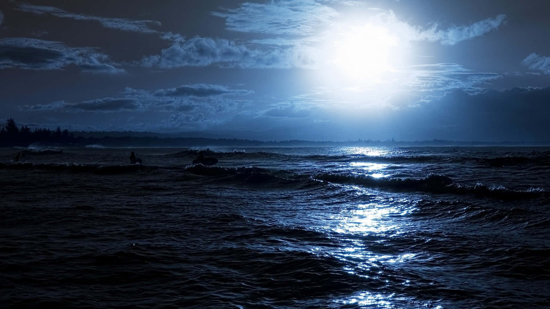 Pretty Ocean 桌布 壁紙 — 月光在陰暗的夜空下閃爍在黑暗的海浪上，遠處有衝浪者的剪影。