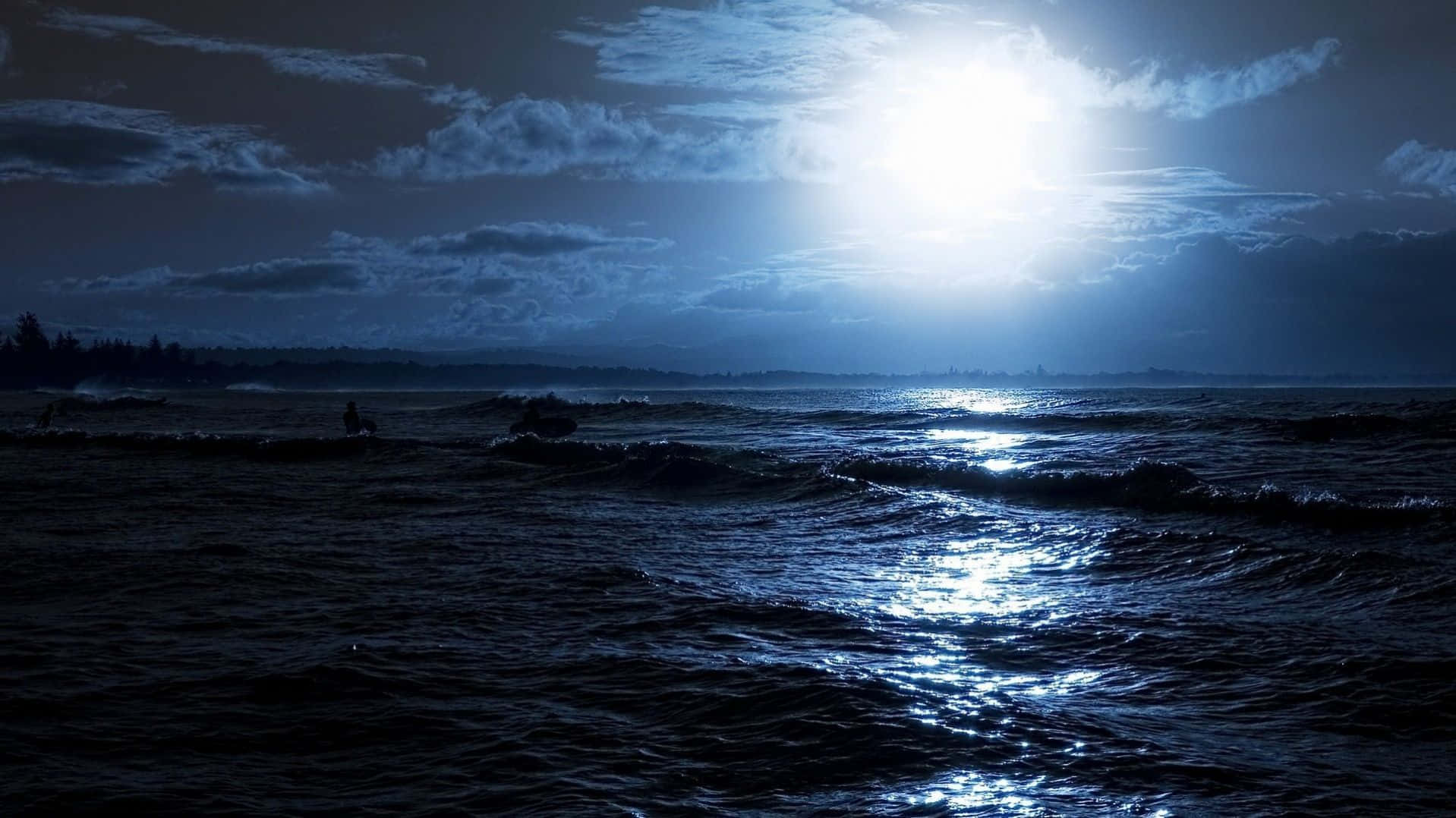 Dark Ocean 桌布 壁紙 — 月光在陰暗的夜空中閃爍在黑暗的海浪上，遠處有衝浪者的剪影。