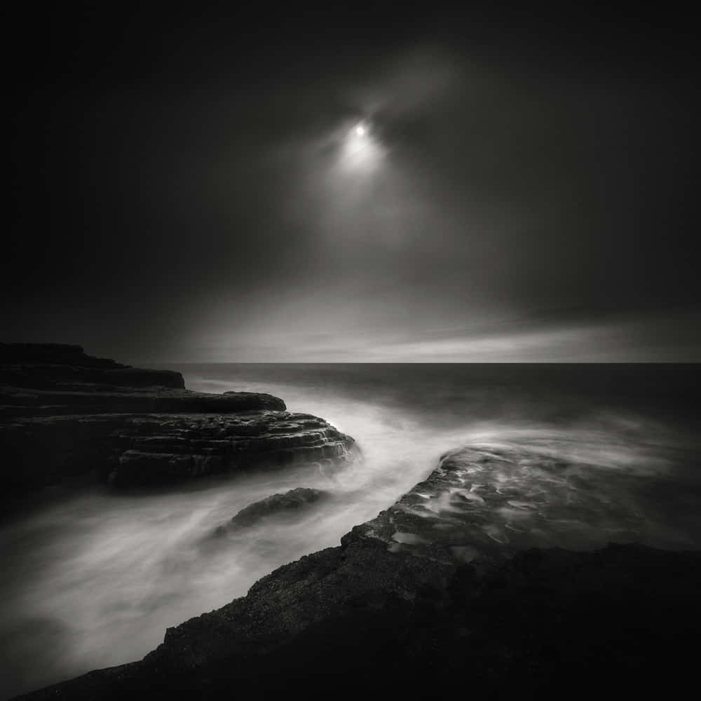 黑色 桌布 壁紙 — 月光穿透烏雲，在霧氣瀰漫的海浪拍打崎嶇懸崖之上投下空靈的光芒。