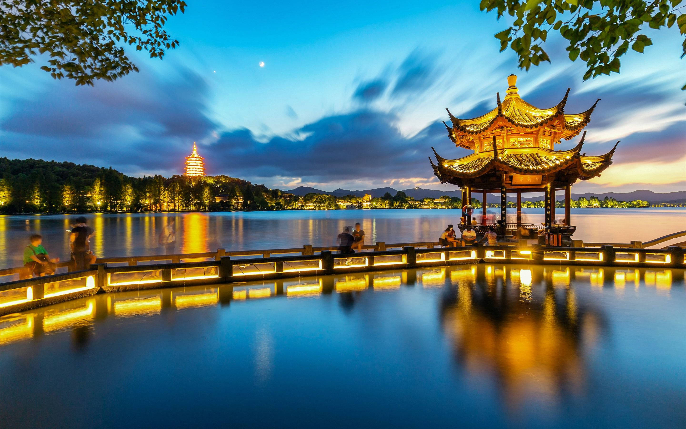 Hangzhou 桌布 壁紙 — 月夜下，平靜湖面倒映著發光的傳統亭閣和遠處寶塔，一片寧靜的黃昏湖邊景色。