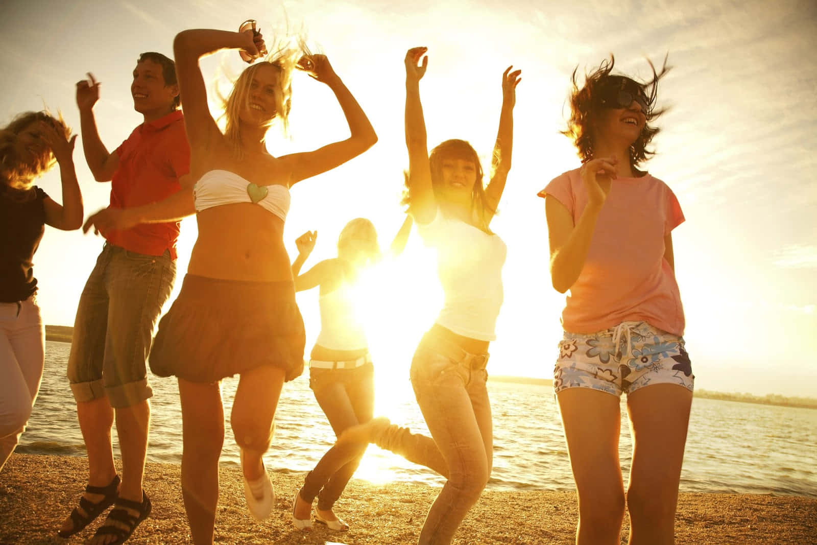Beach Party 桌布 壁紙 — 朋友們在沙灘上歡快地跳舞，金色夕陽的光芒在他們身後閃耀。