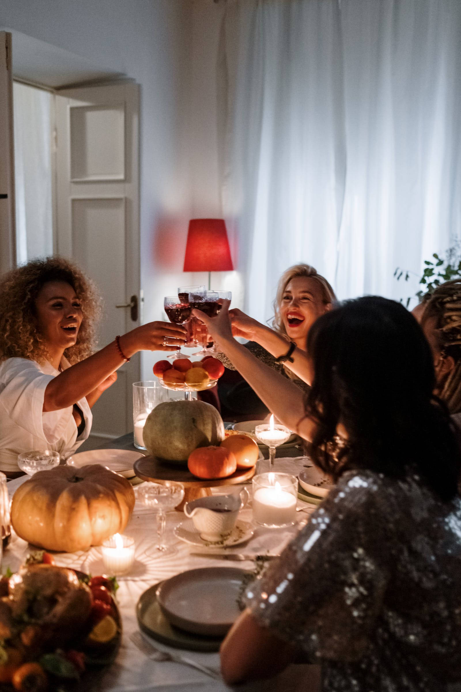 Thanksgiving Day 桌布 壁紙 — 朋友們在溫暖燈光的秋季晚餐桌上歡笑並用葡萄酒乾杯，桌上裝飾著南瓜和蠟燭。