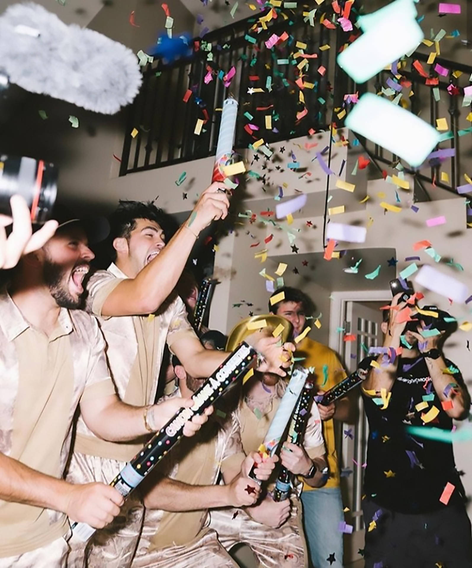 party 桌布 壁紙 — 朋友們穿著緞面睡衣在室內慶祝，彩紙炮噴出彩色紙片和星星。