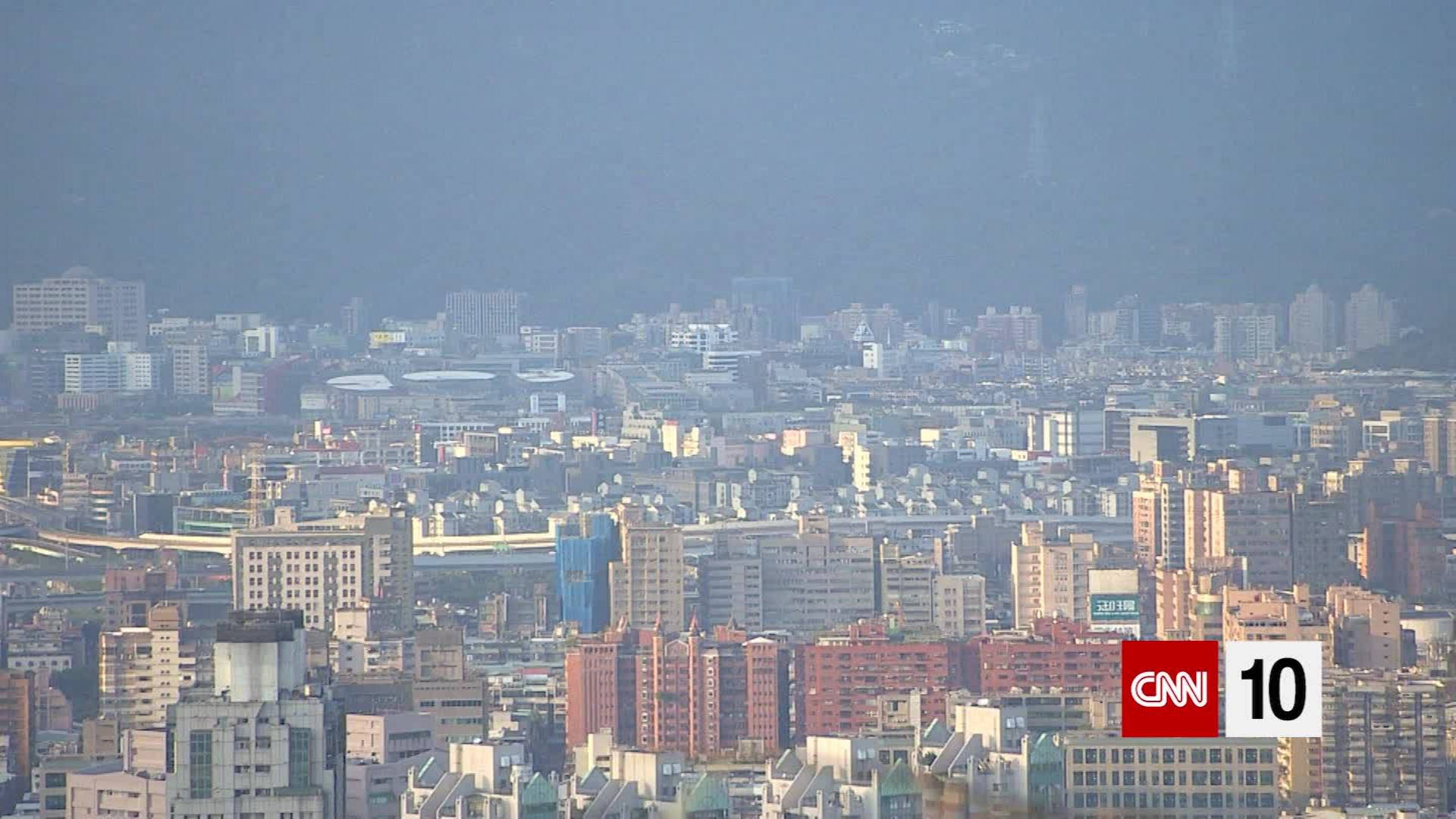 View 桌布 壁紙 — 朦朧的城市天際線，密集的建築物和遠處的山脈，在柔和的天空下。