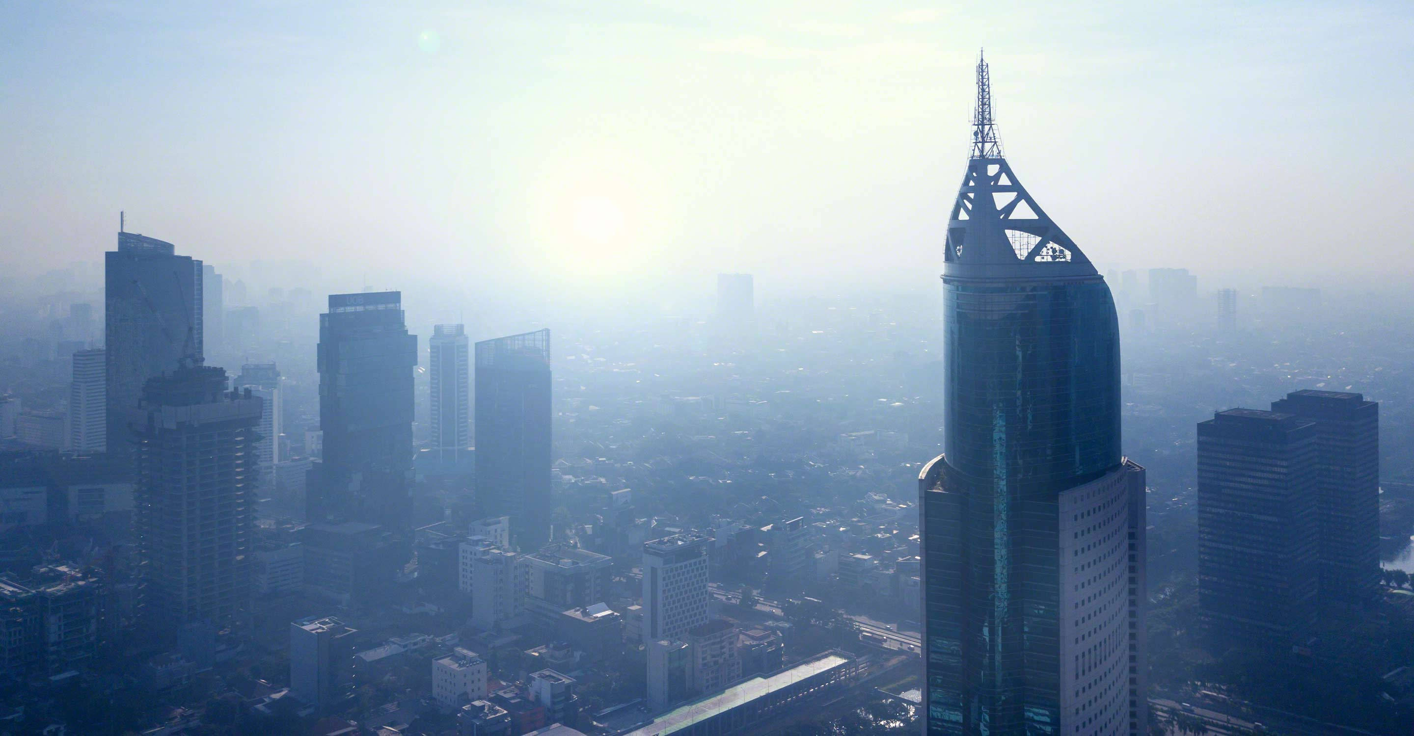 Jakarta 桌布 壁紙 — 朦朧的城市天際線沐浴在柔和晨光中，一座高聳的玻璃摩天大樓佔據了前景。