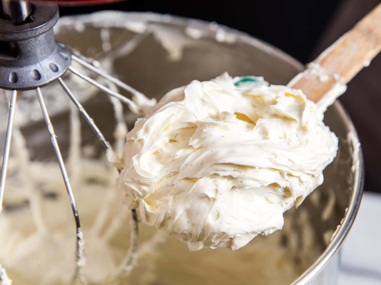 Buttercream 桌布 壁紙 — 木勺從帶有打蛋器配件的不鏽鋼攪拌碗中舀起濃稠的奶油香草豆糖霜。