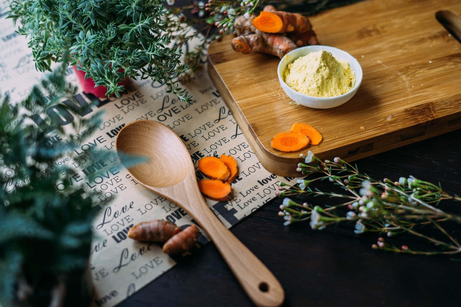Spices 桌布 壁紙 — 木匙放在新鮮薑黃根和粉末旁邊，置於質樸木板上，伴有綠色植物和愛情主題紙張。