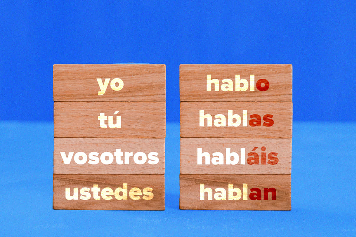 Spanish 桌布 壁紙 — 木塊在鮮豔的藍色背景上展示西班牙語代詞和變位動詞。