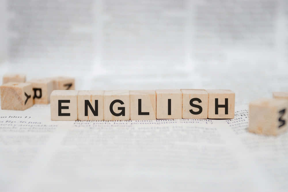 English 桌布 壁紙 — 木塊拼出「ENGLISH」字樣，置於模糊的報紙頁面上，光線柔和自然。