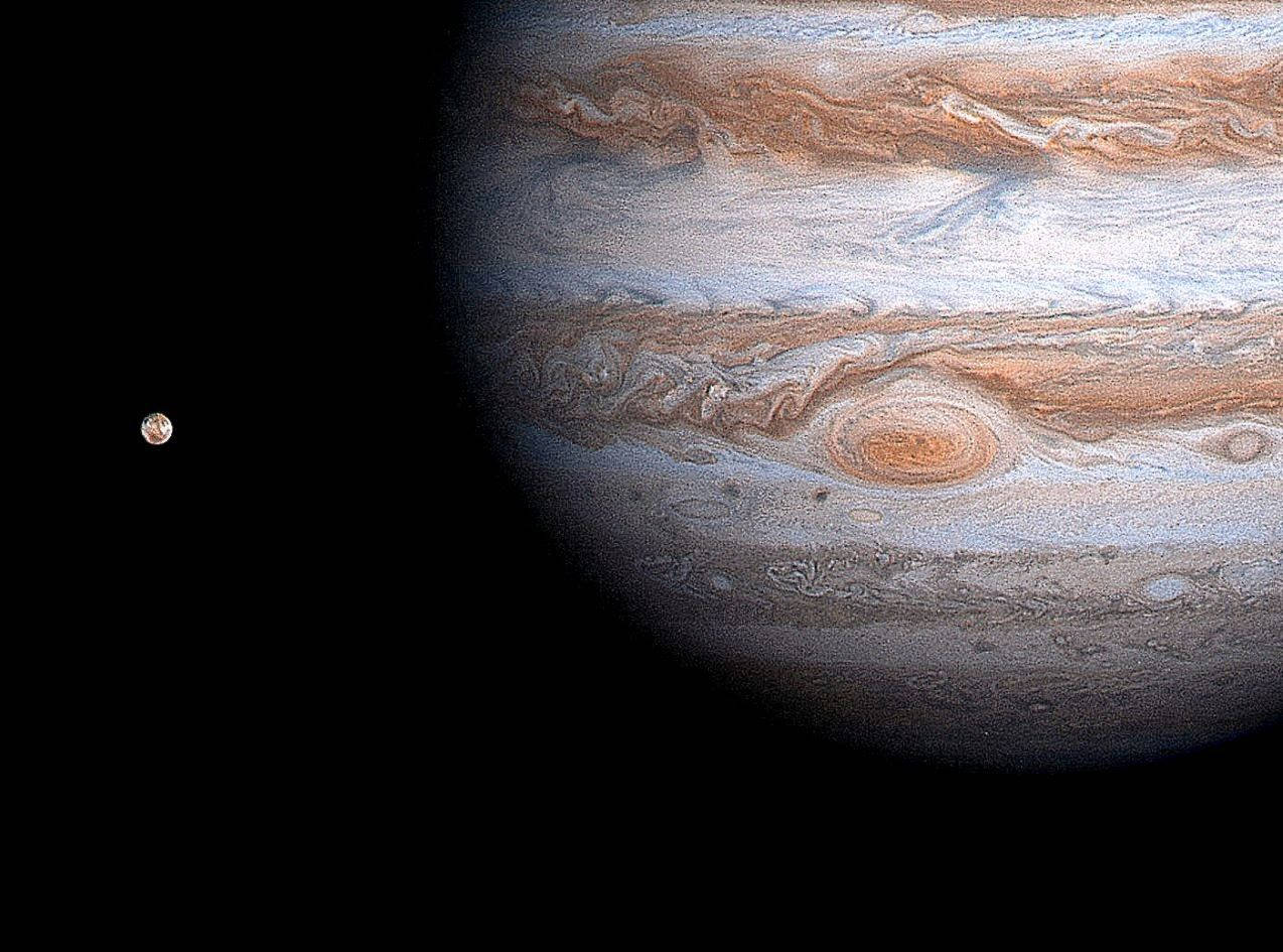 木星 桌布 壁紙 — 木星主導畫面，呈現橙色、白色和棕色的漩渦狀條紋，一顆小衛星在附近的黑色太空虛空中發光。
