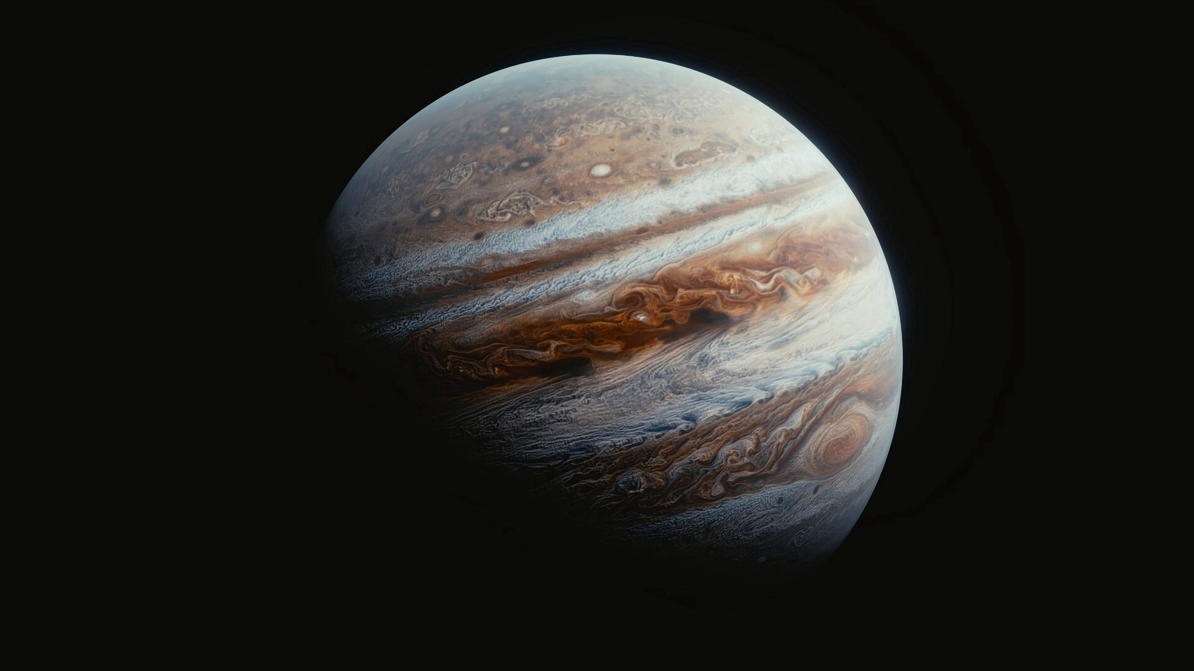 外太空 桌布 壁紙 — 木星在虛空中顯得巨大，其米色、棕色和白色的雲帶旋轉，被遠處的光照亮。