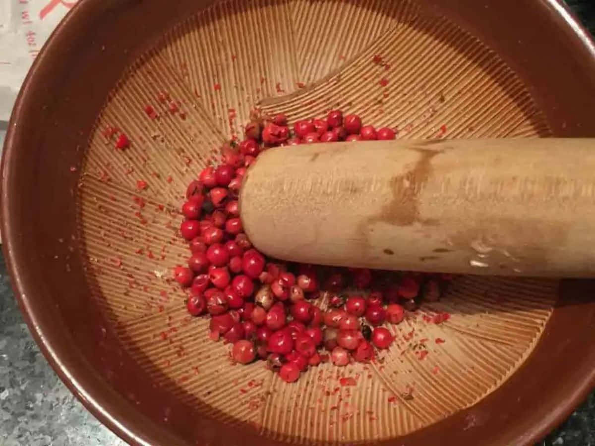 Pink Peppercorn 桌布 壁紙 — 木杵在帶有放射狀凹槽的赤陶研缽中碾碎鮮紅的胡椒粒。