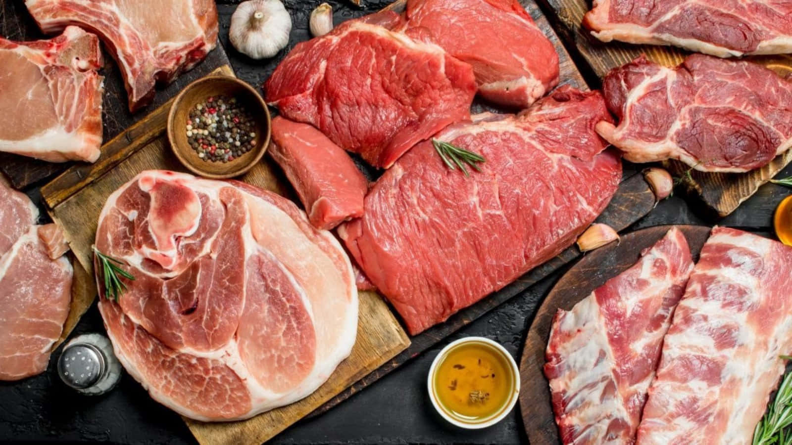 meat 桌布 壁紙 — 木板上擺放著各種生紅肉和豬肉塊，搭配大蒜、迷迭香和油，呈現質樸的擺盤。