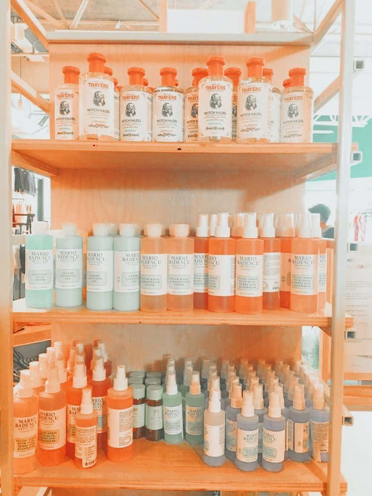Peachy Aesthetic 桌布 壁紙 — 木架上陳列著一排排 Mario Badescu 和 Thayers 的護膚品瓶，呈現柔和溫暖光線下的粉彩和橙色調。