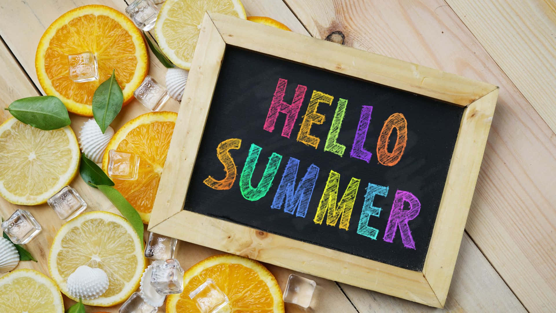 夏天 桌布 壁紙 — 木框黑板，上面有彩虹色的「HELLO SUMMER」文字，周圍環繞著柑橘片、冰塊和貝殼，放在淺色木質表面上。