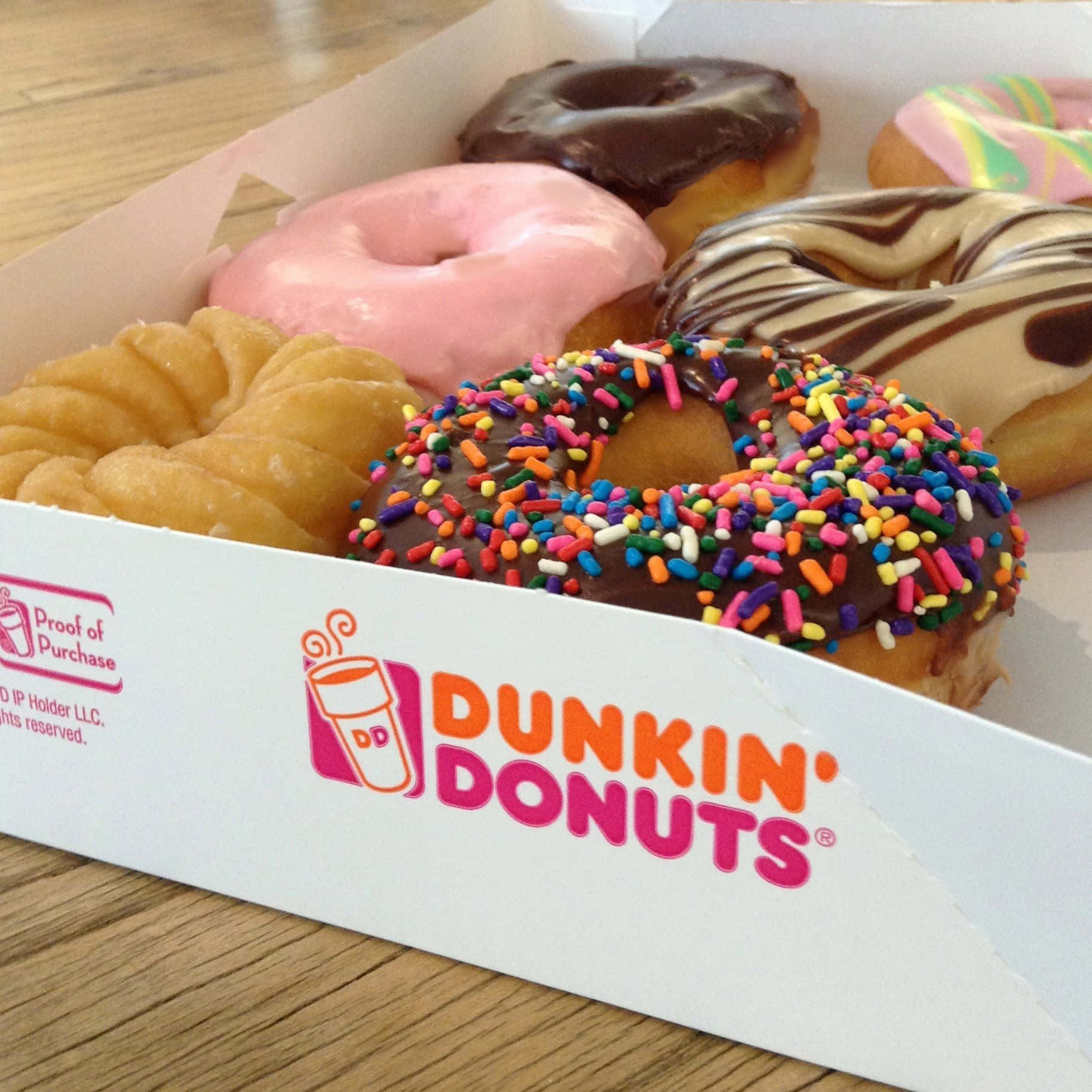 Dunkin Donuts 桌布 壁紙 — 木桌上品牌盒內各種色彩繽紛的Dunkin' Donuts糕點特寫。