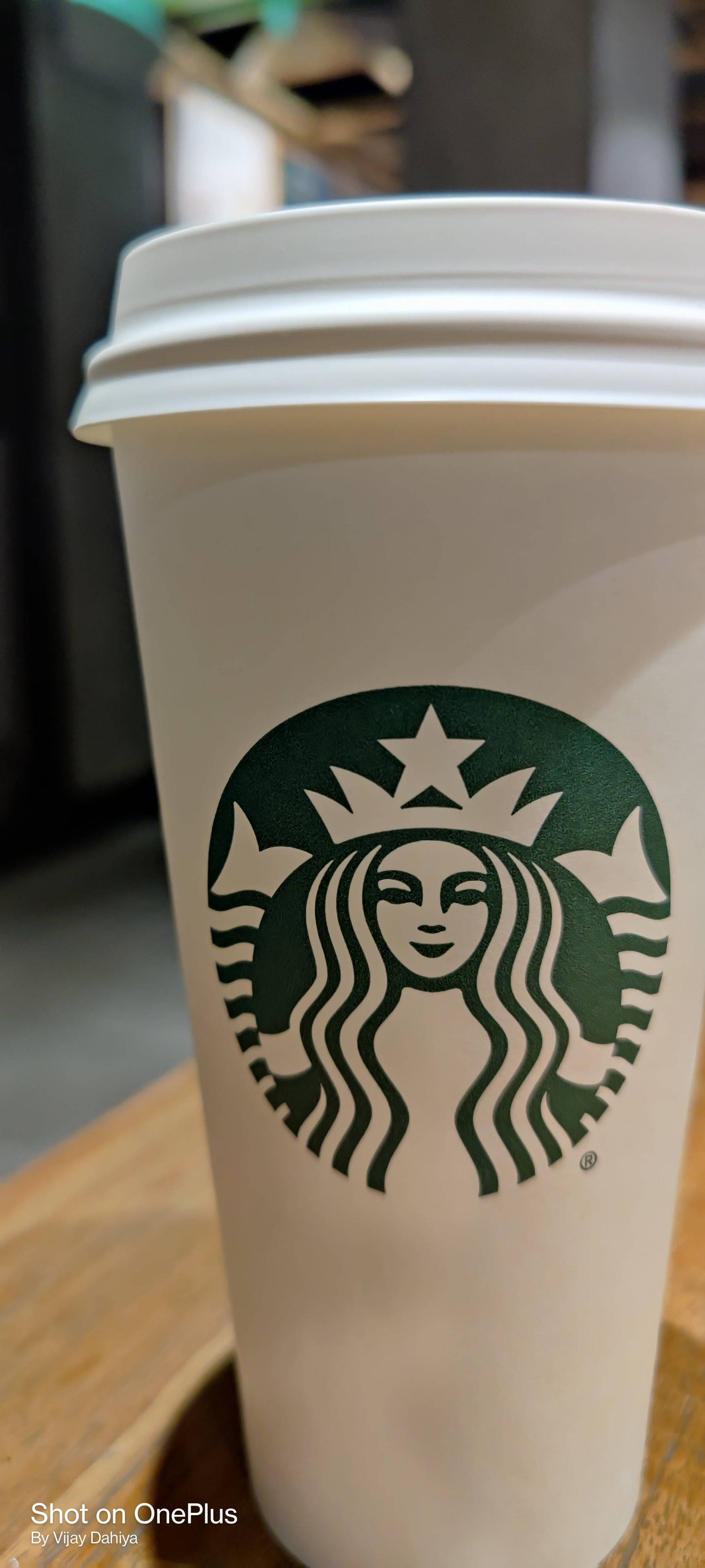 白色Starbucks咖啡杯，帶有綠色標誌，置於木桌上。 — 星巴克 GIF 壁紙
