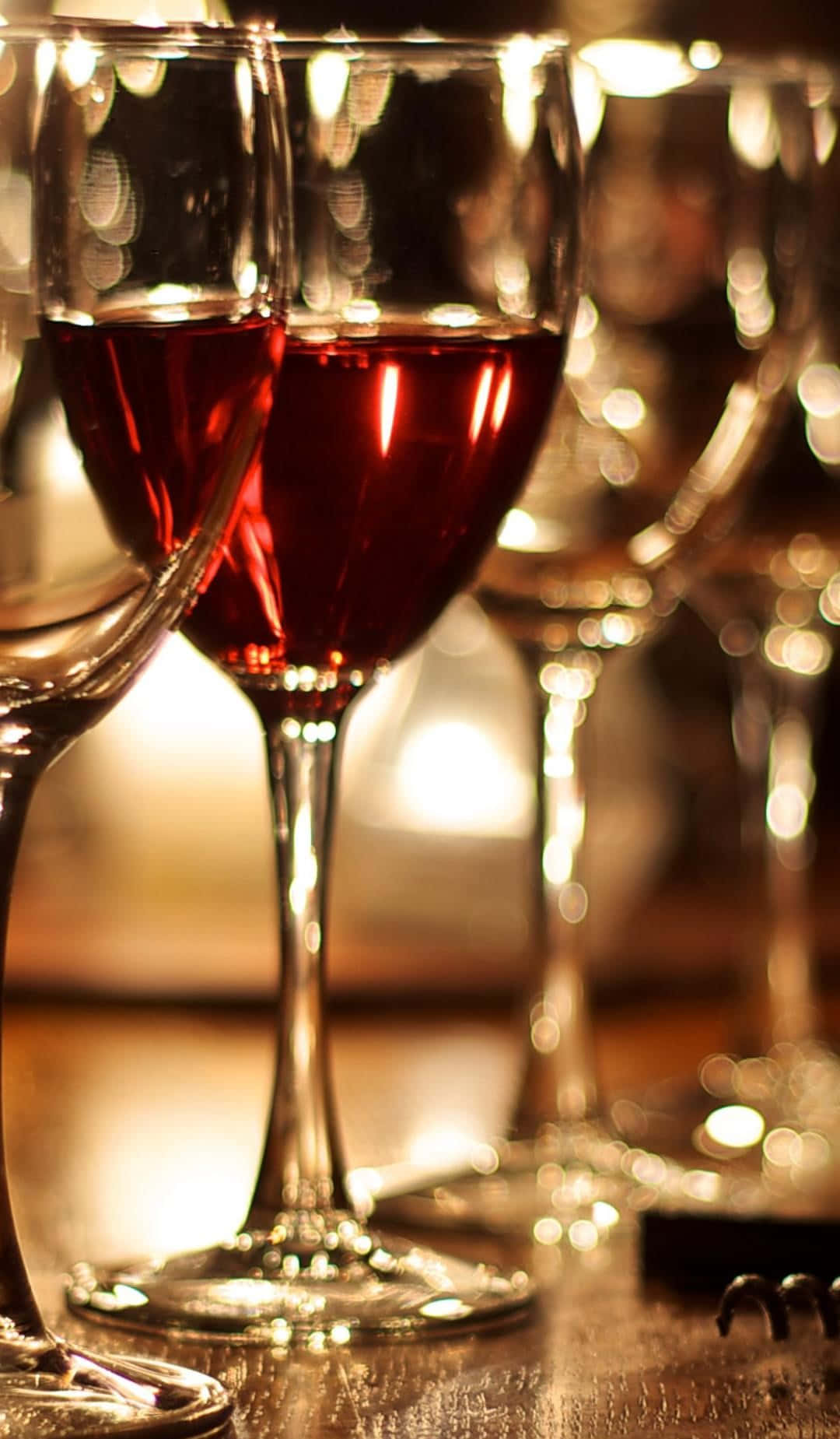 Red Wine Glass 桌布 壁紙 — 木桌上盛滿紅酒的酒杯在柔和金色燈光下溫暖發光的特寫。