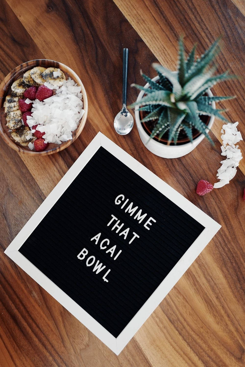 Healthy Food 桌布 壁紙 — 木桌的俯視圖，有一個字母板寫著 gimme that acai bowl，旁邊有一碗上面有覆盆子和椰子片的巴西莓碗。
