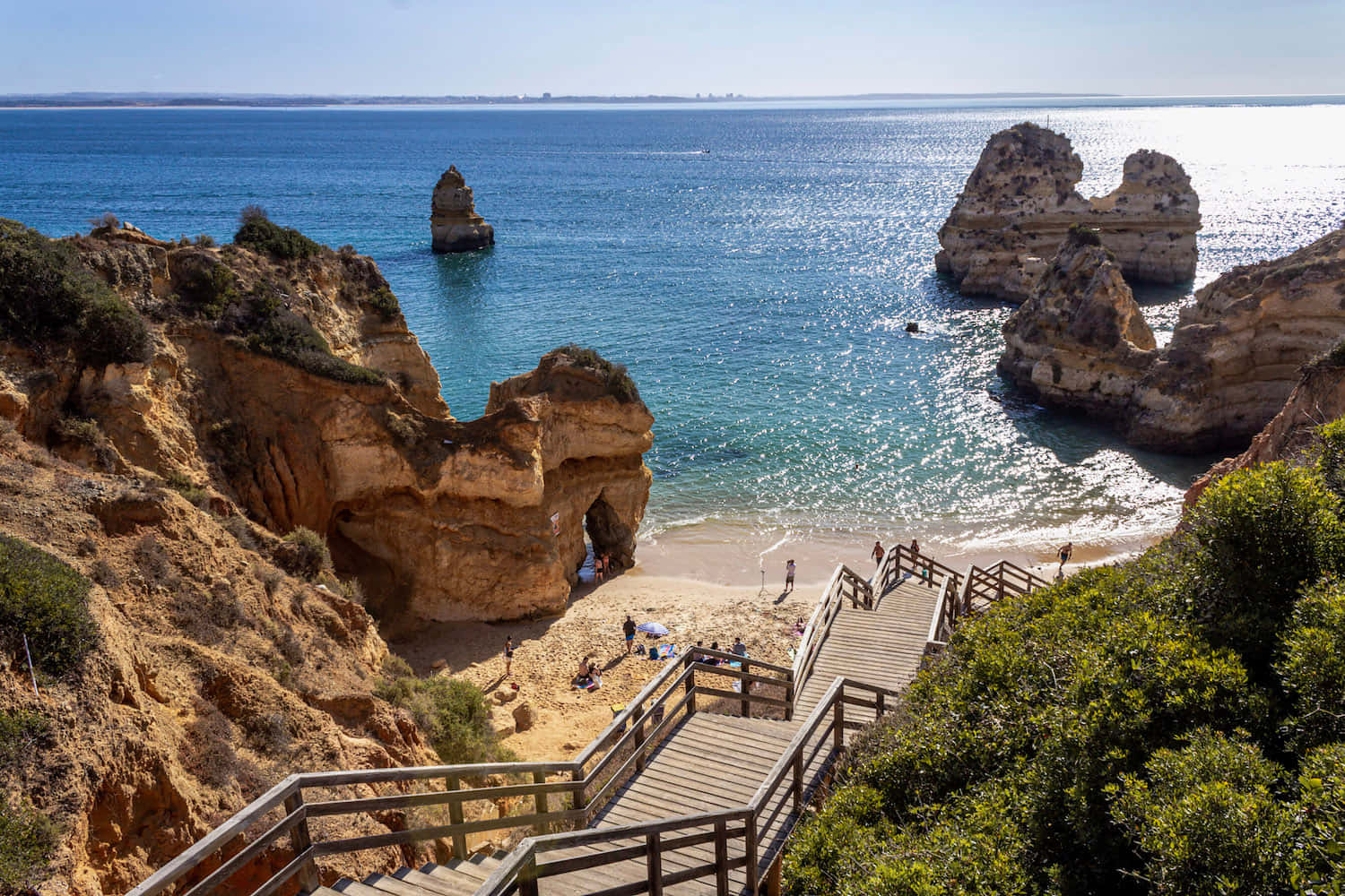 Portuguese Beach 桌布 壁紙 — 木樓梯向下延伸至一個陽光明媚的海灘，四周環繞著崎嶇的懸崖和碧綠色的海洋，並有岩石 formations。