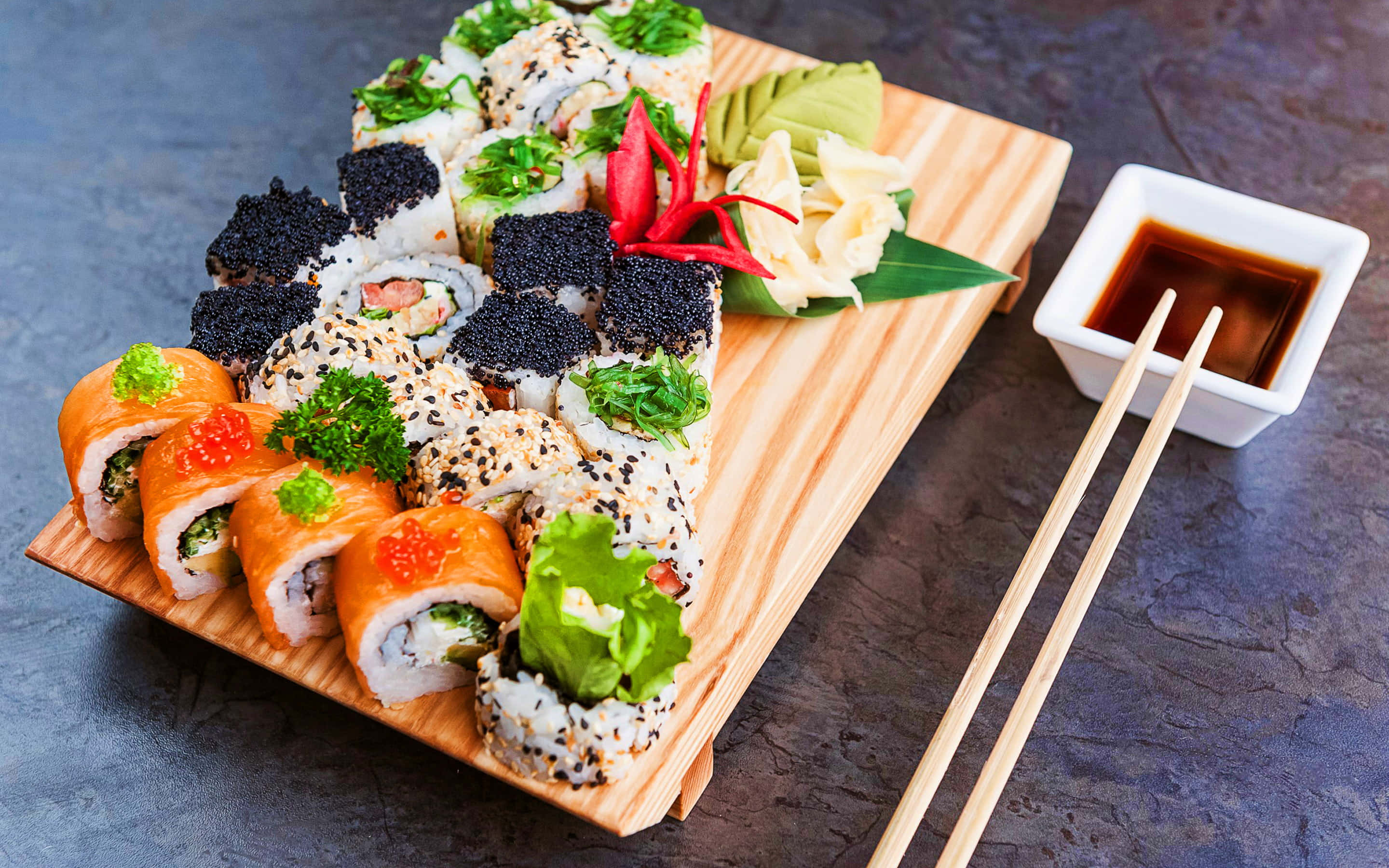 Platter 桌布 壁紙 — 木盤上展示各種壽司卷，上面放有飛魚籽、芝麻、酪梨和紅魚子醬，旁邊有醬油和筷子。