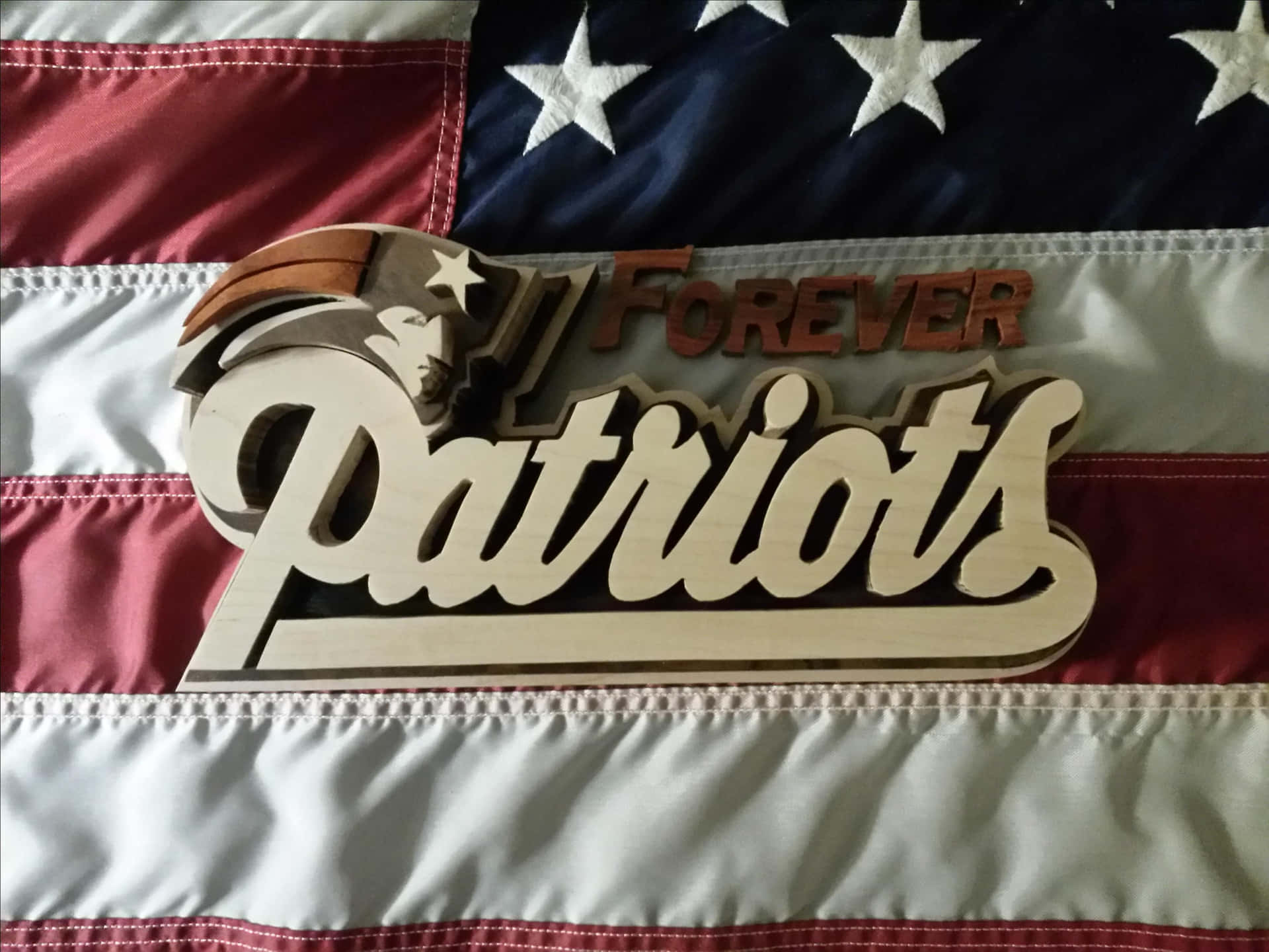 壁紙 — 木製 'Forever Patriots' 標誌連頭盔標誌放在摺疊的美國國旗上。