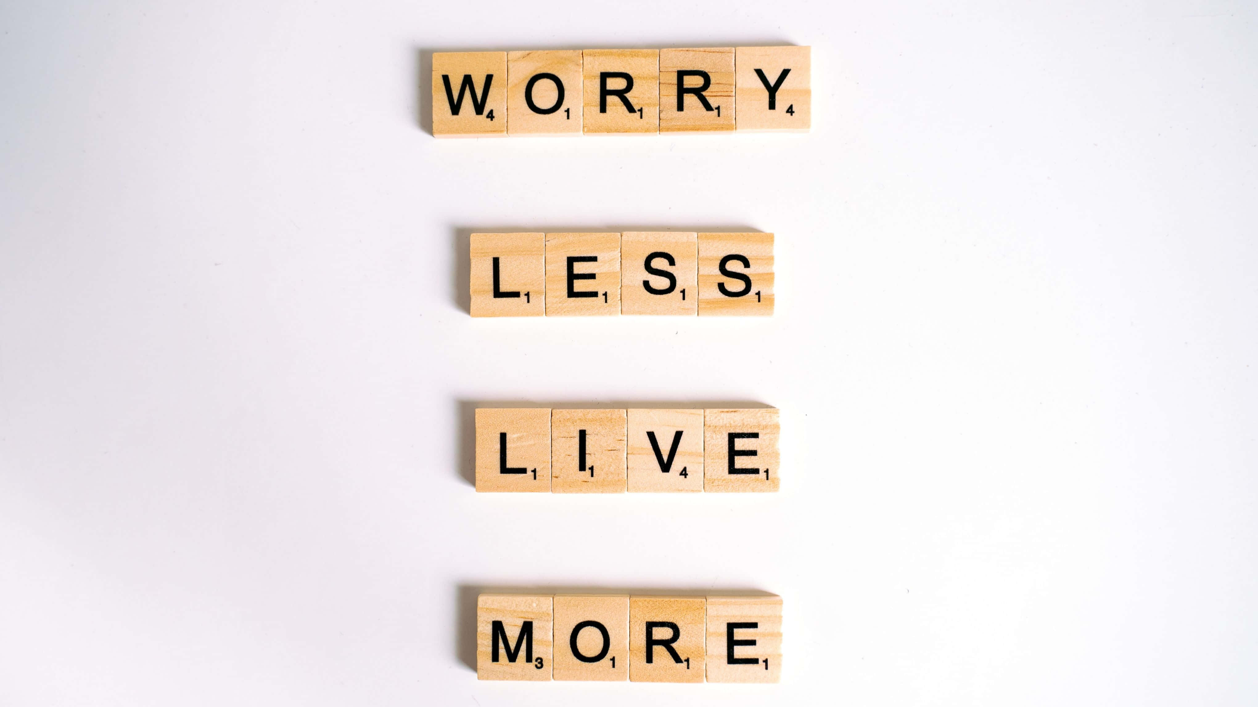 語錄 桌布 壁紙 — 木製 Scrabble 字塊垂直拼出 'WORRY LESS LIVE MORE'，背景為純白色。