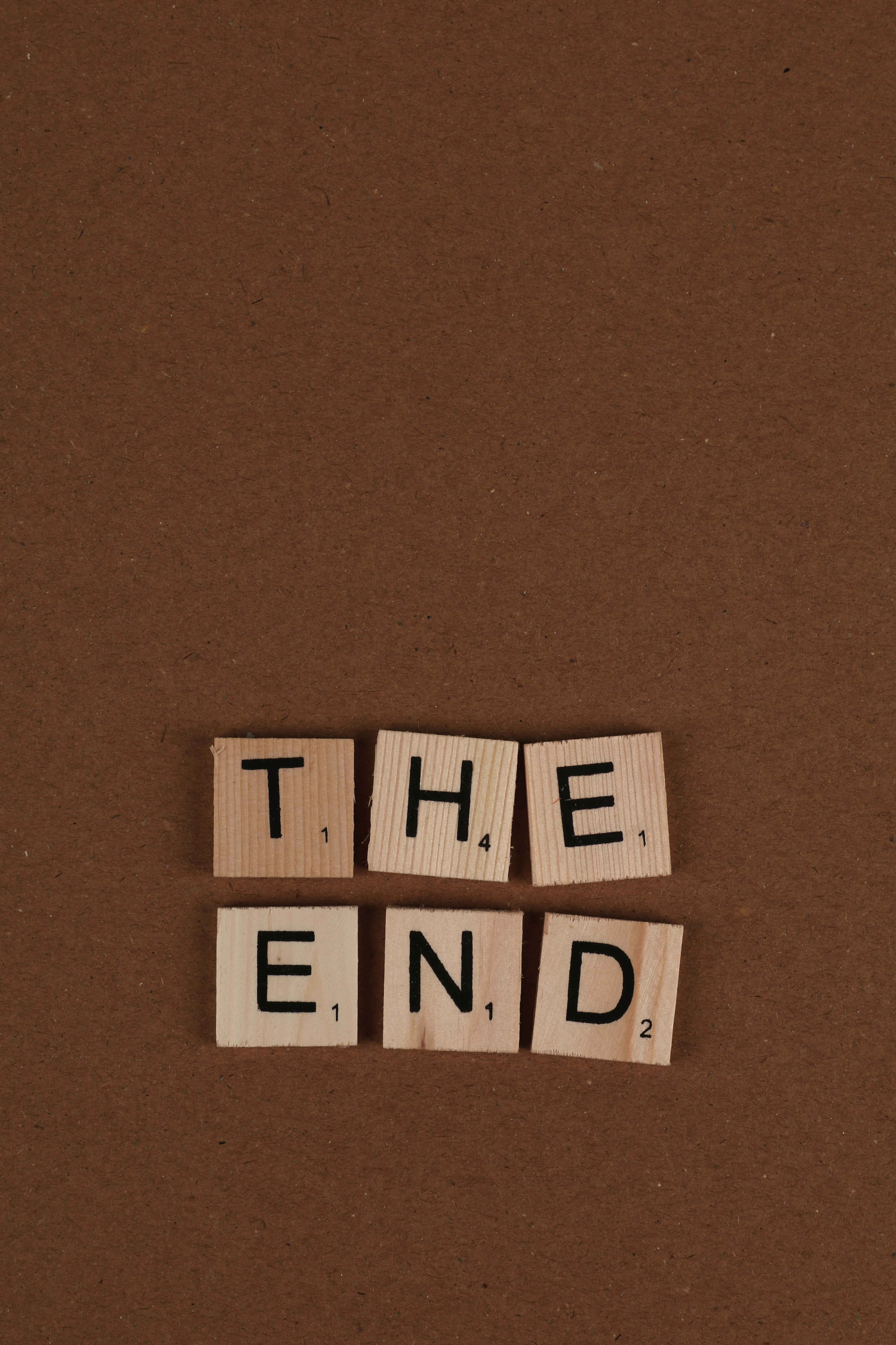 the end 桌布 壁紙 — 木製 Scrabble 字塊拼出 'THE END'，居中放置在帶紋理的棕色表面上。