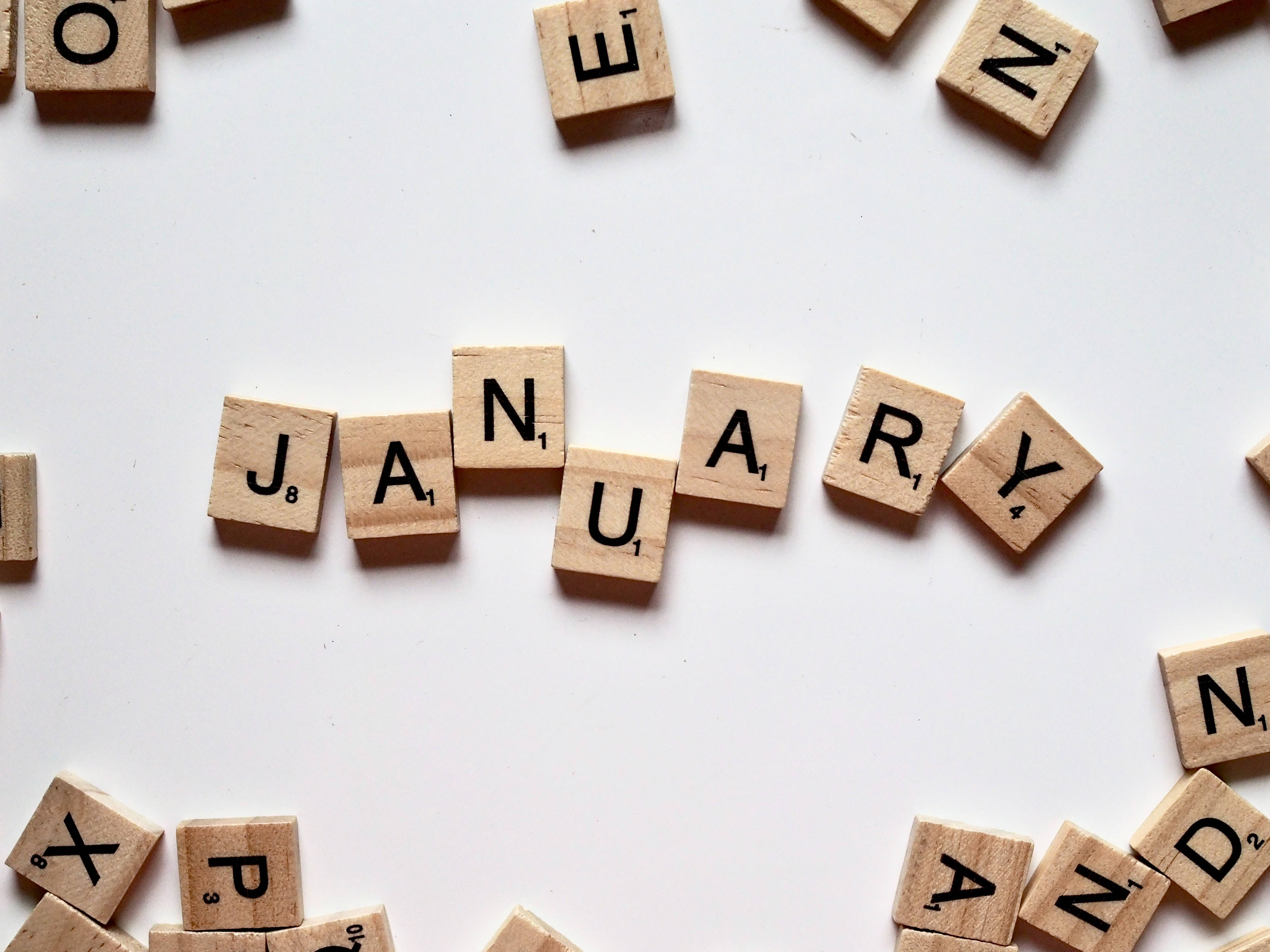 一月 桌布 壁紙 — 木製 Scrabble 字母塊在潔白背景上拼出「一月」，周圍散落著字母。