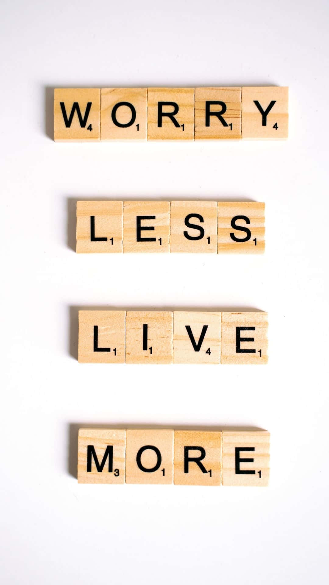語錄 桌布 壁紙 — 木製 Scrabble 字母塊在純白背景上垂直拼出 'WORRY LESS LIVE MORE'。