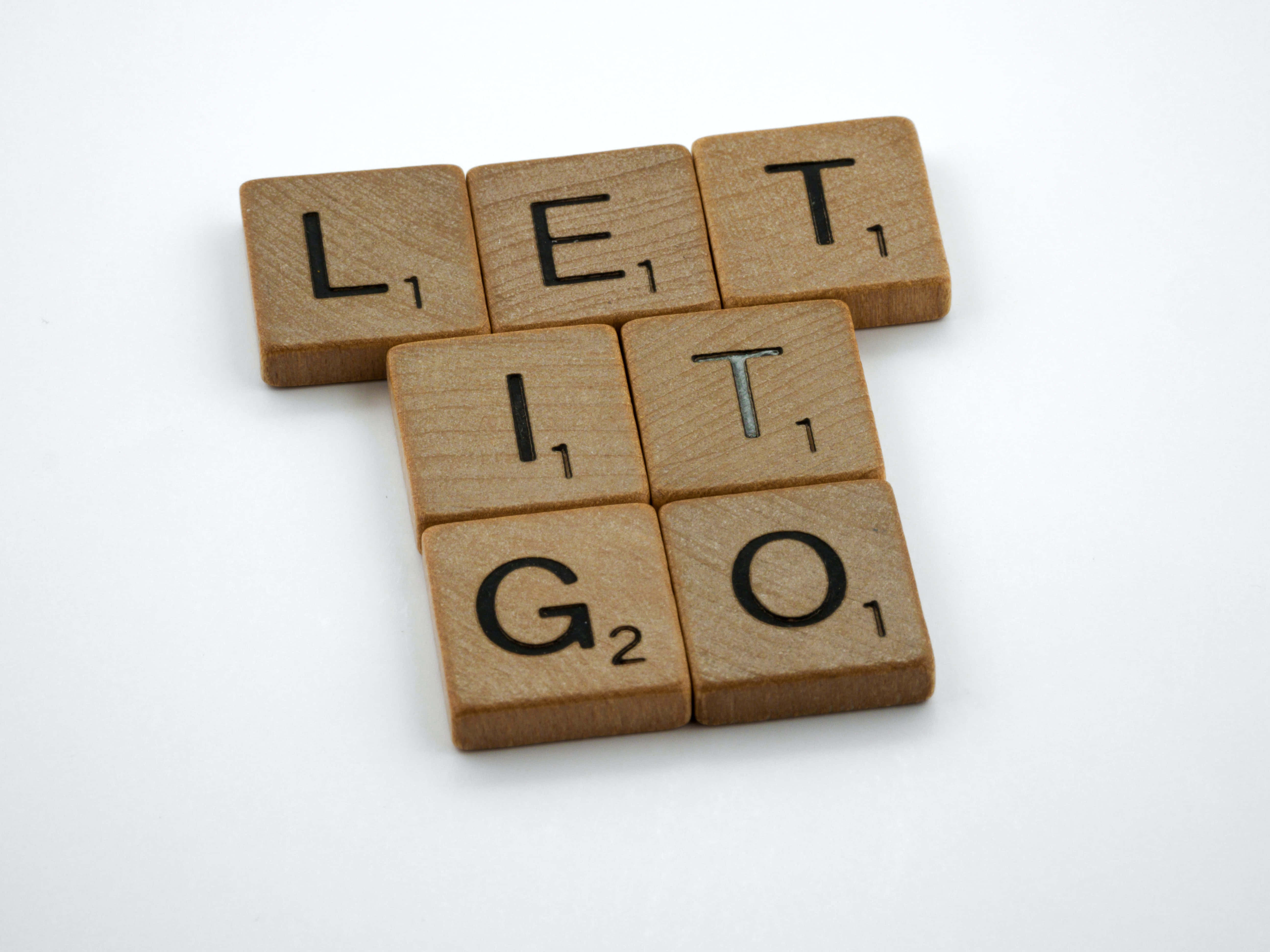 let it go 桌布 壁紙 — 木製 Scrabble 字母塊拼出 LET IT GO，以 T 形排列在純白色背景上。